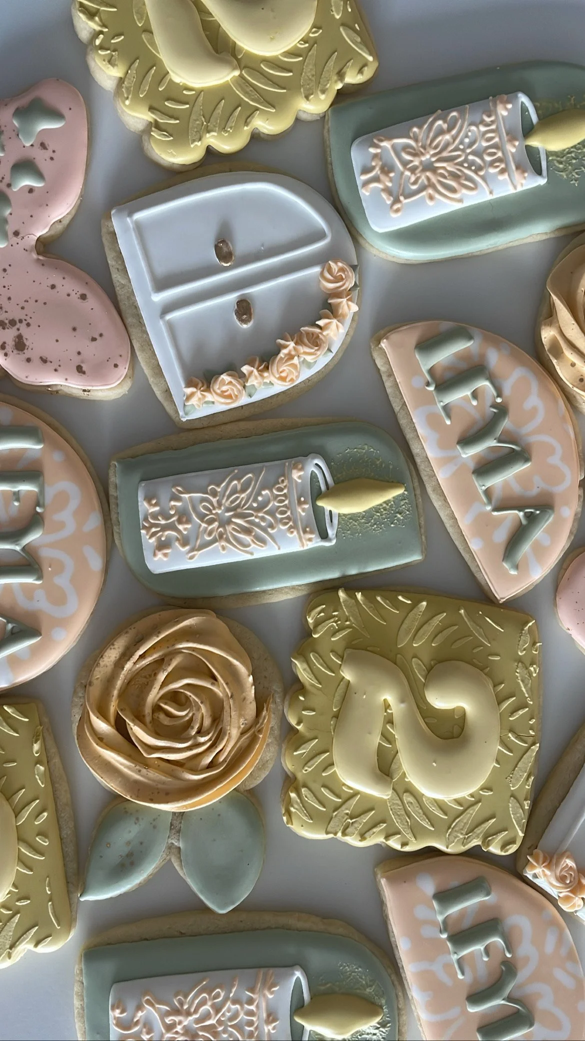 Assorted decorated cookies in pastel colors, including a cookie shaped like a piano, roses, and abstract designs with icing detailing.