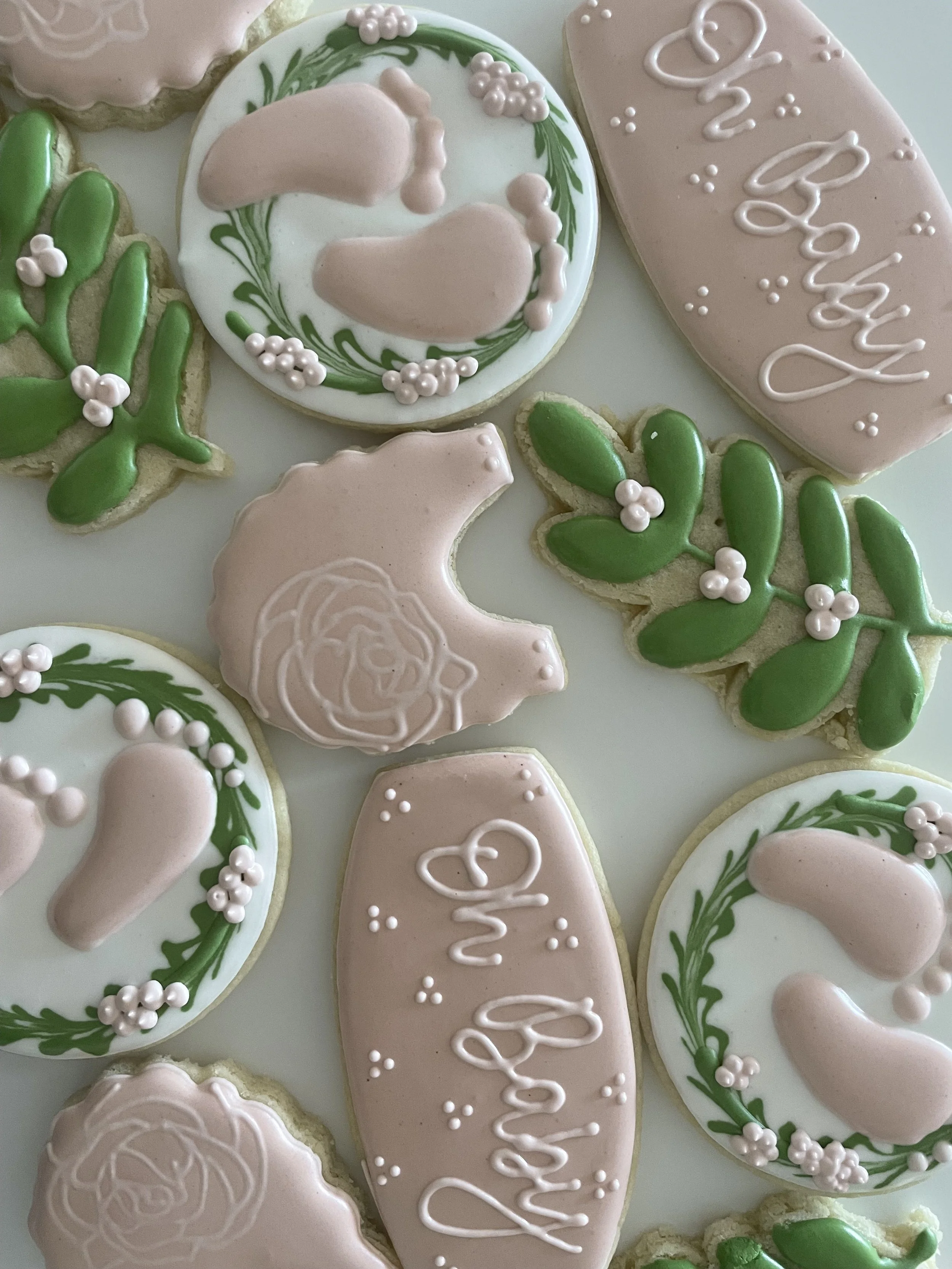 Assorted Christmas cookies decorated with pastel pink, white, and green icing, including cookies with the words "Merry" and "Xmas" written on them, and designs of holly leaves and berries.