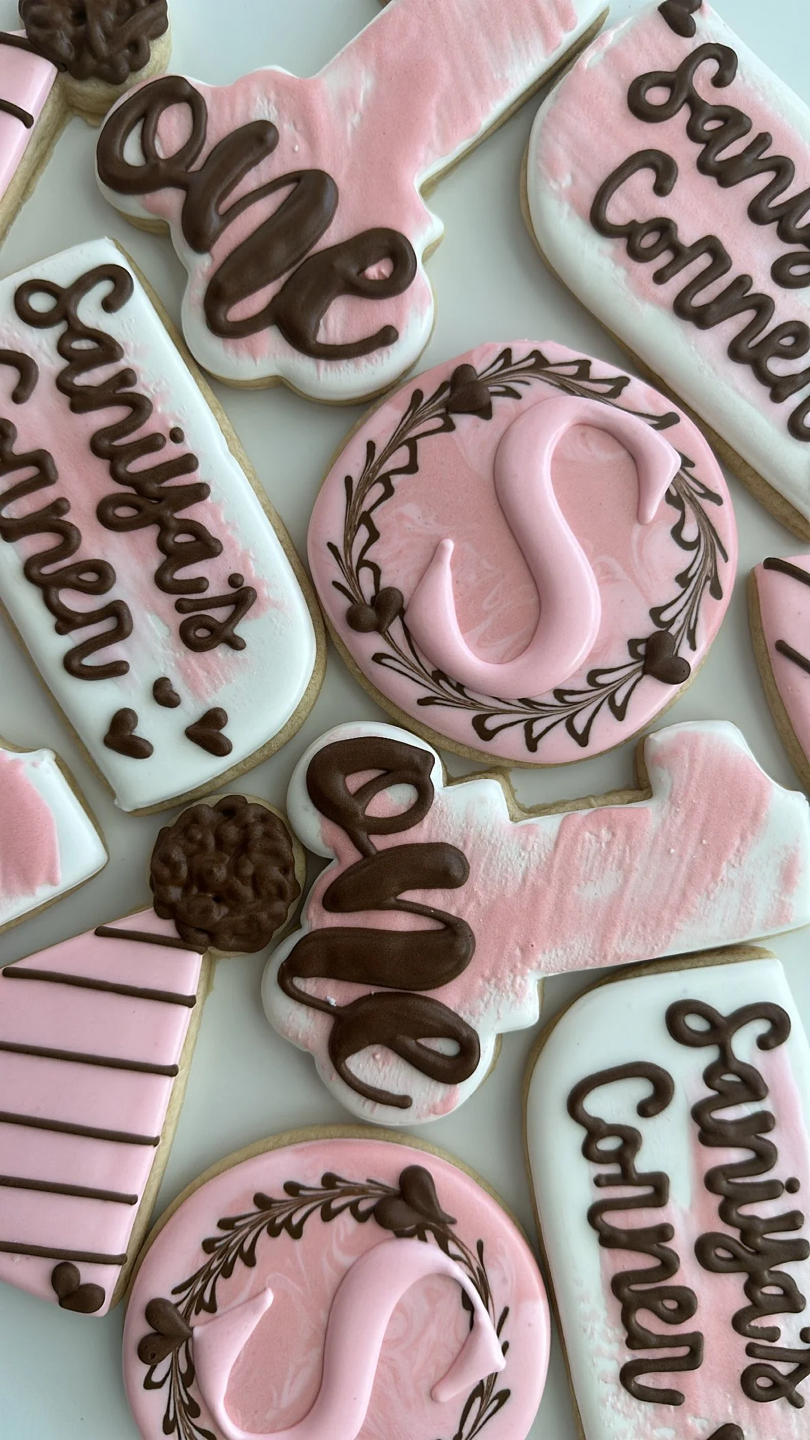 Decorated cookies with pink and white icing, some with words and others with decorative designs, arranged on a surface.