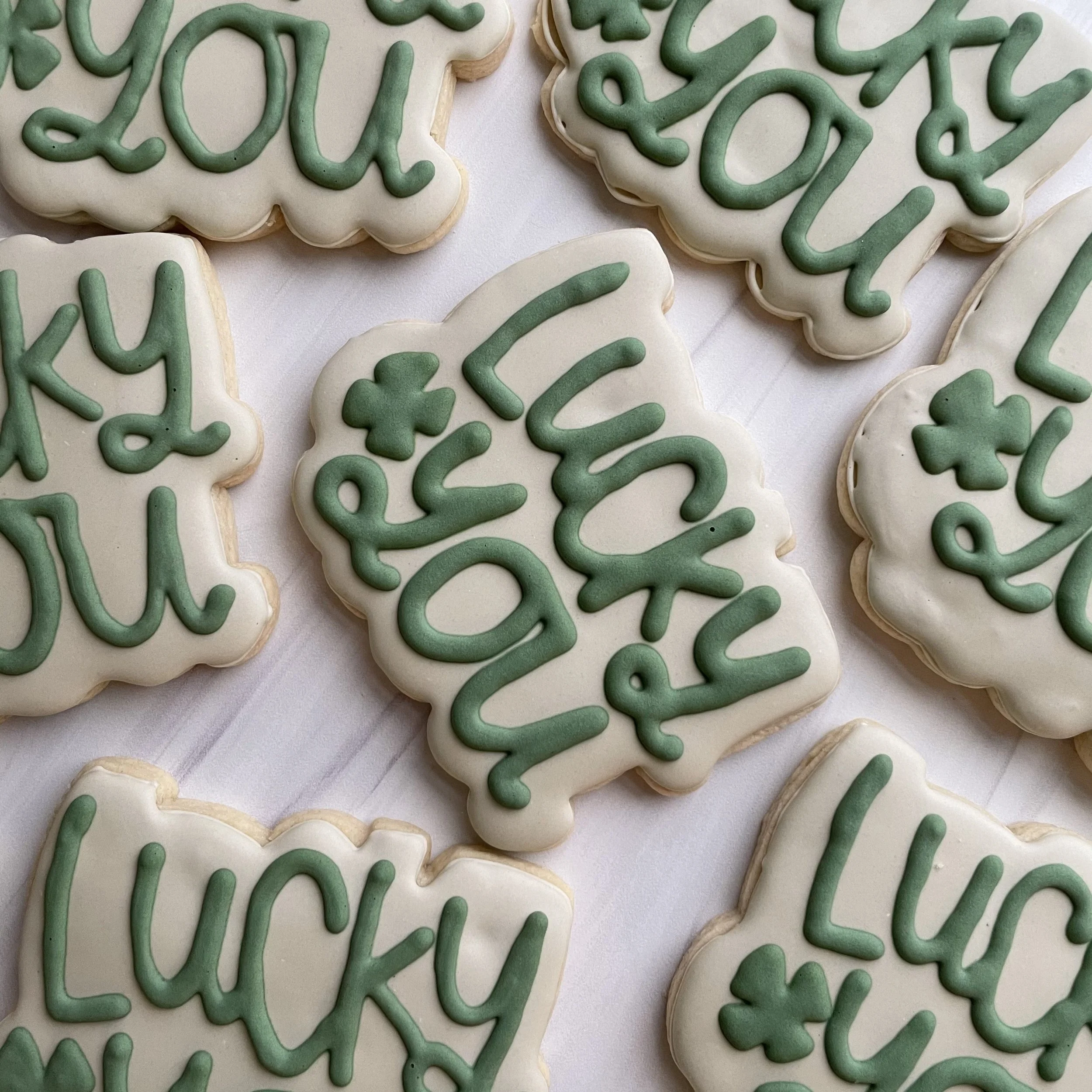 Close-up of decorated sugar cookies with white icing and green icing writing.
