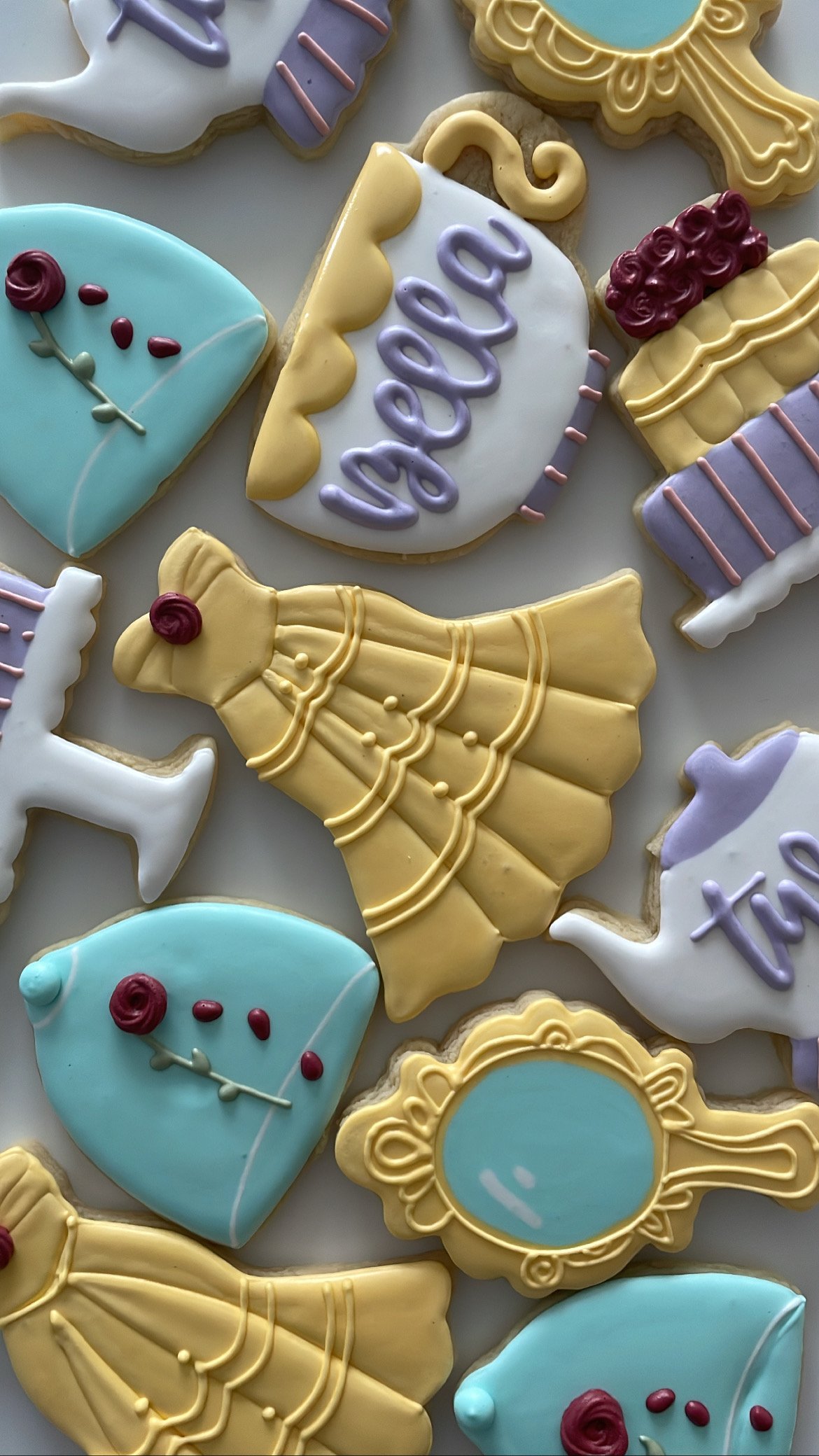 Decorated cookies in pastel colors resembling dresses, shoes, and ornate frames, with the word 'baby' written on one.