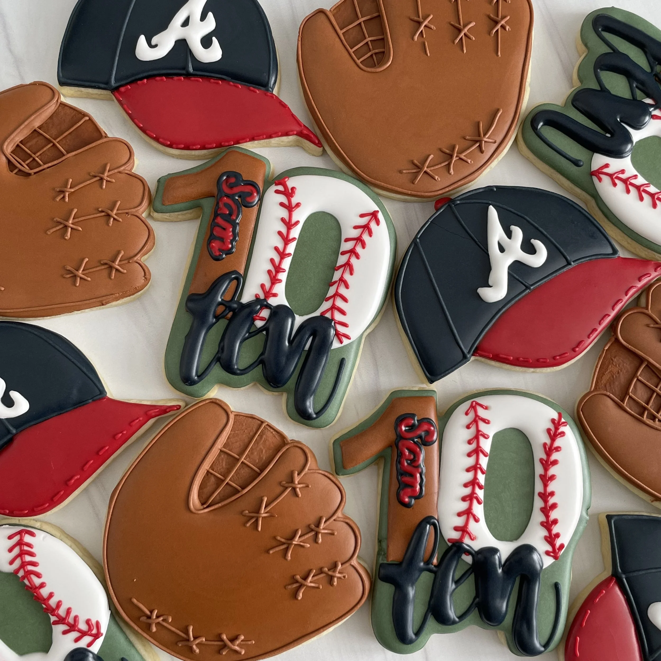 Decorated baseball-themed cookies, including a baseball glove, baseball, baseball bat, and baseball helmet, with colorful icing and lettering.