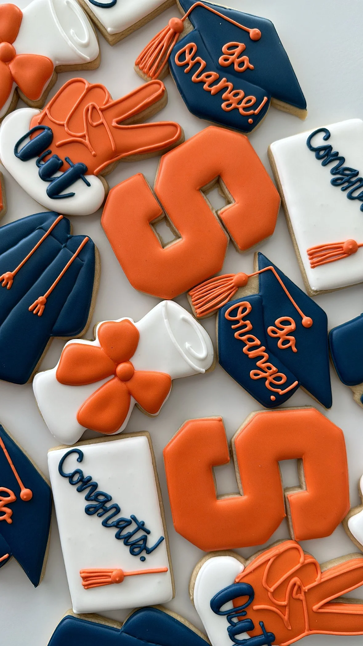 Decorated cookies with graduation theme including a mortarboard cap, a diploma, a graduation cap with the word 'Congratulations!', and orange and navy blue accents.