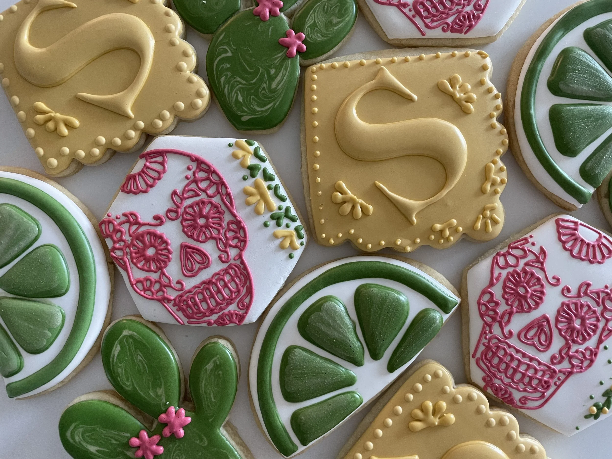 Decorated sugar cookies with green, white, pink, and yellow icing featuring hearts, flowers, and abstract designs.
