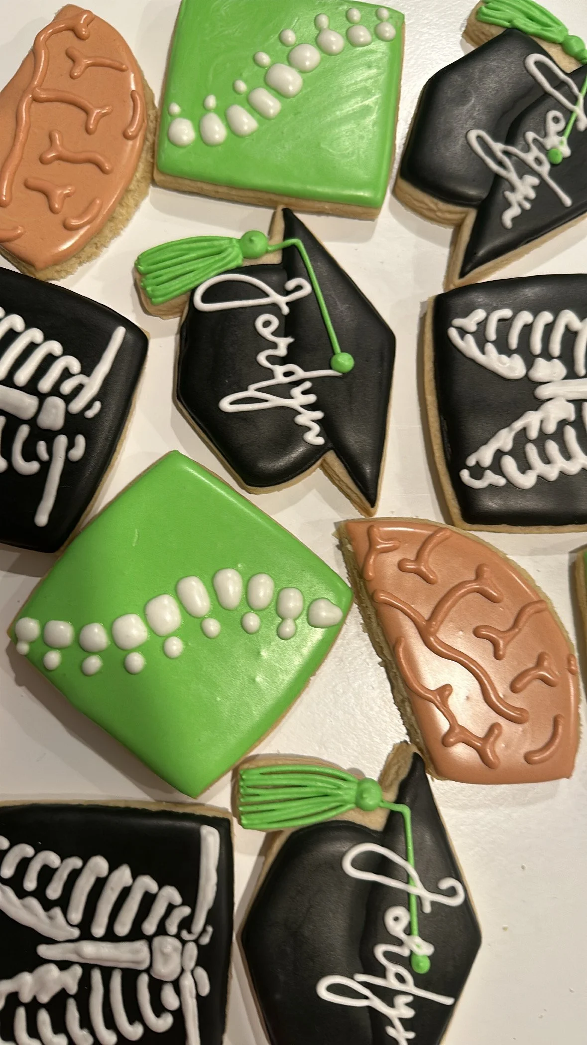 Assorted decorated cookies with graduation theme, including black and green caps, and messages like 'Graduation' written on some cookies.
