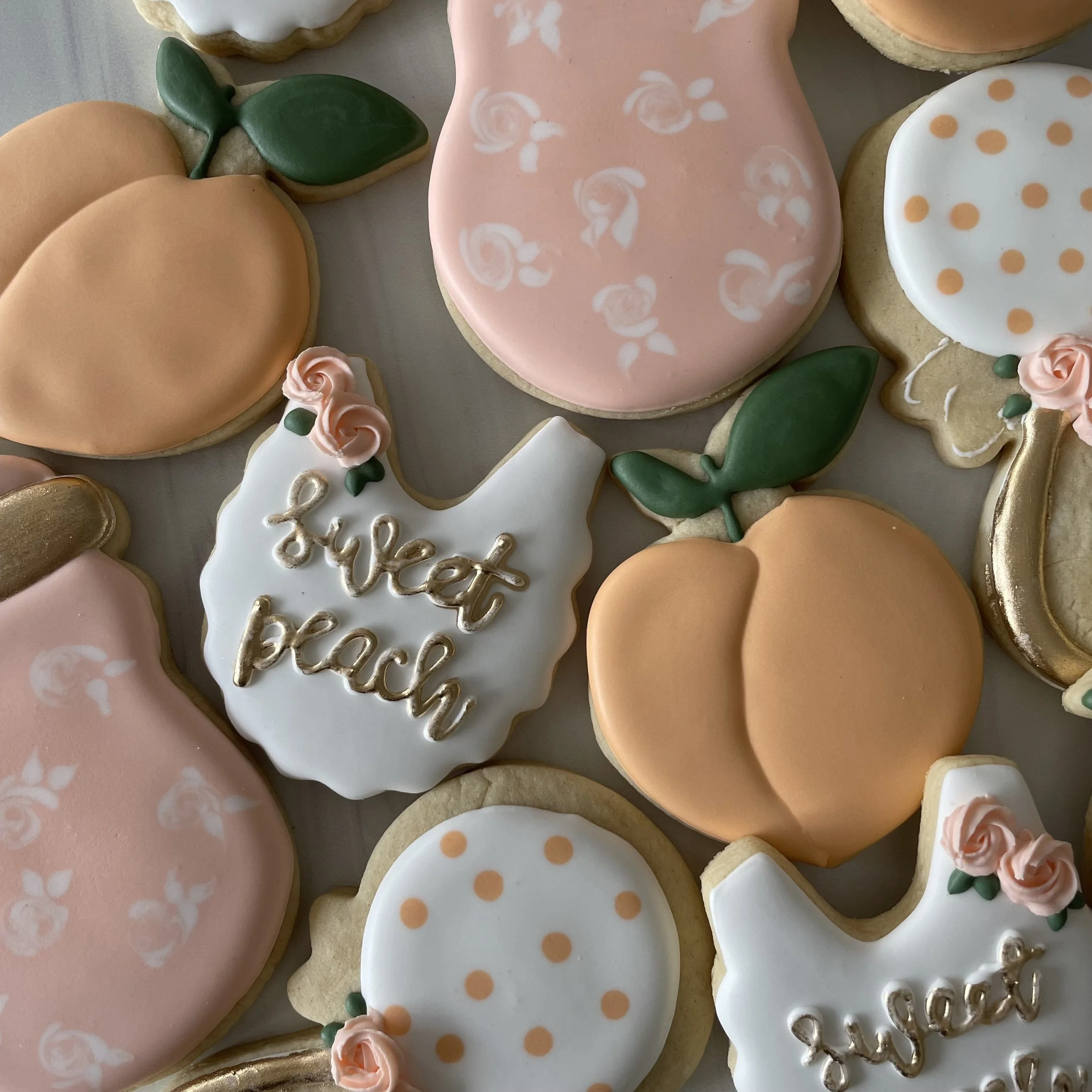 Assorted decorated cookies with various pastel colors, floral patterns, and polka dots, some with pink roses, green leaves, and written messages.