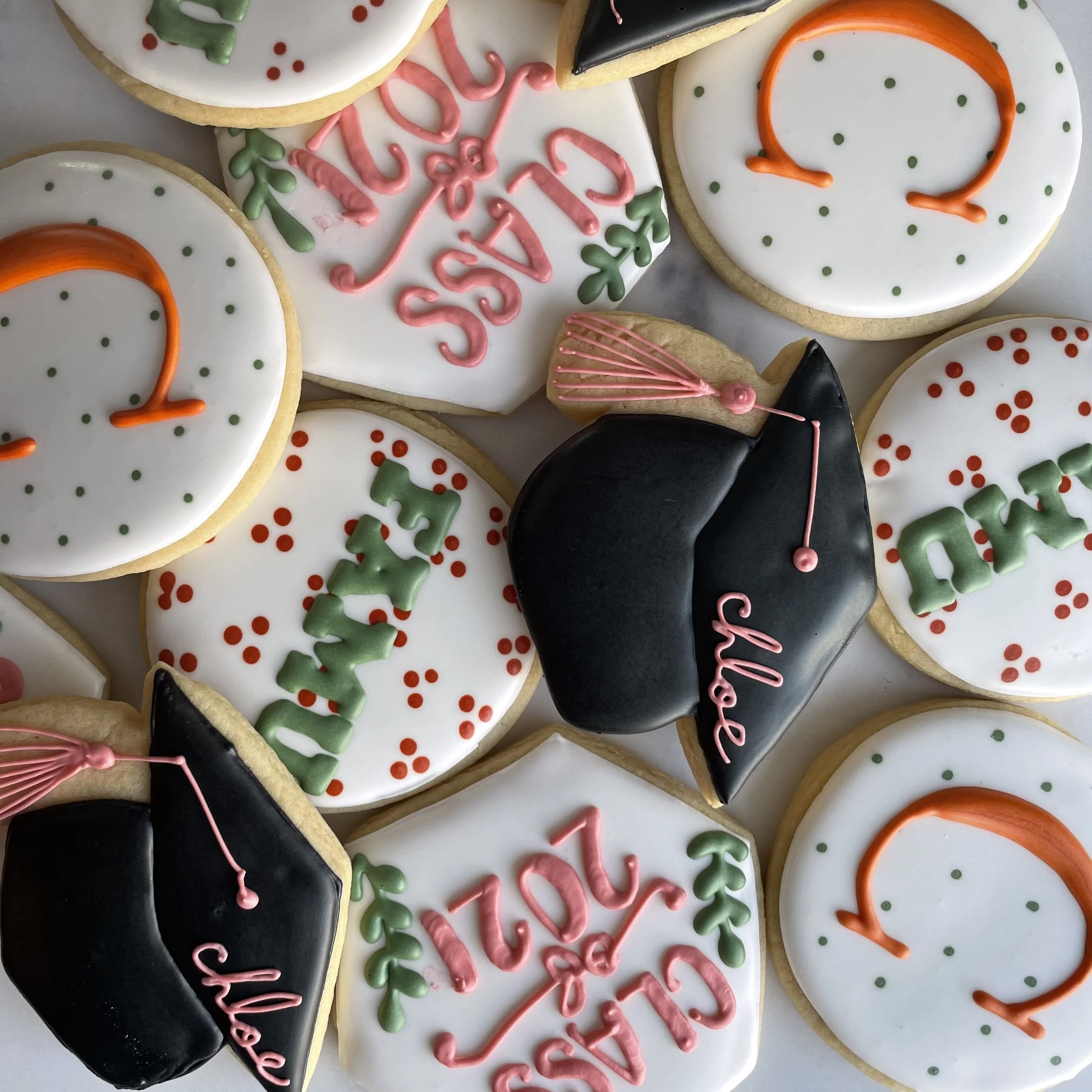Christmas decorated cookies with white, black, and orange icing, pink and green details, and festive messages.