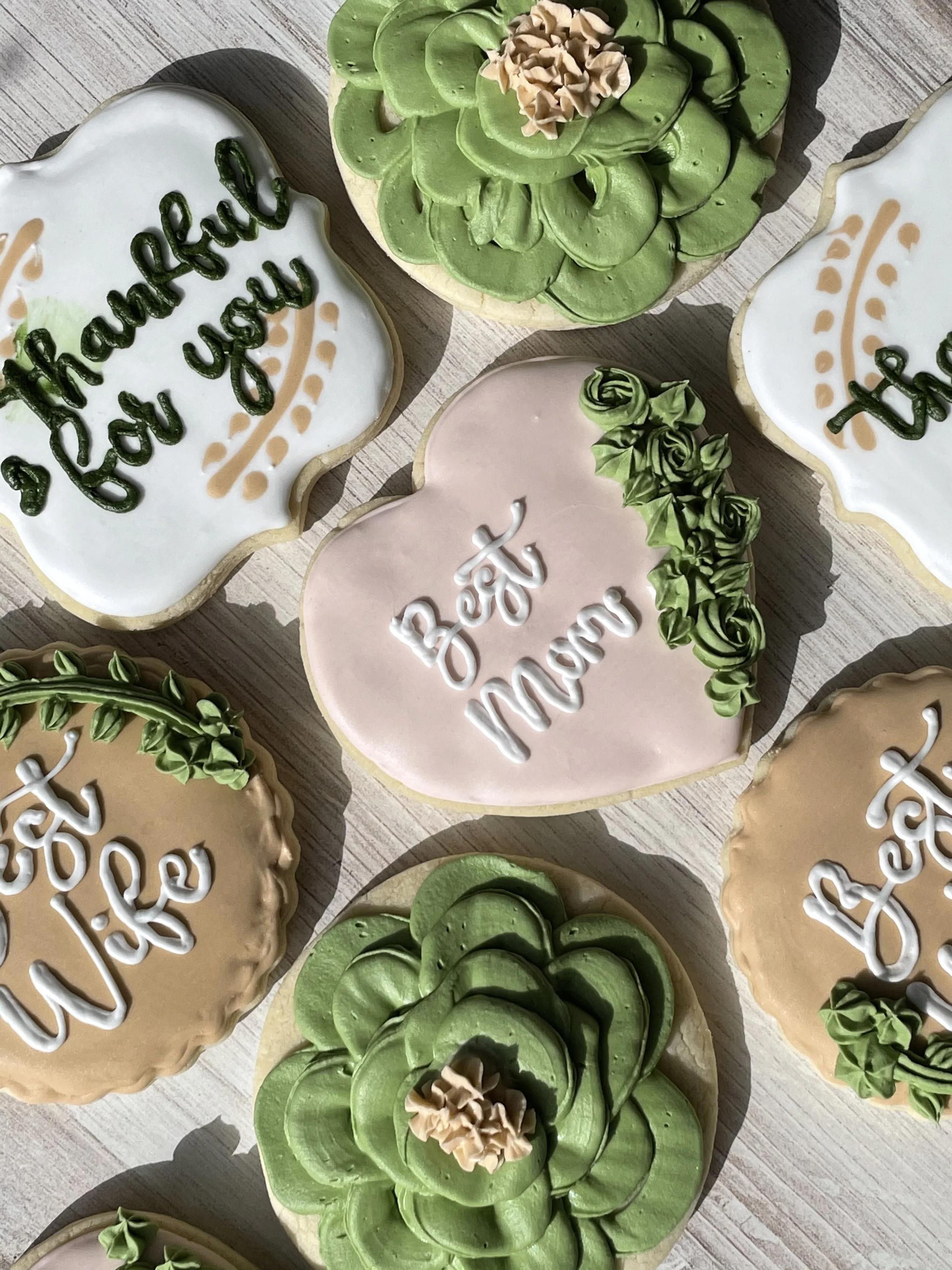 Decorated cookies for a celebration, including one with the message 'Thank You' in green icing, and others with pink and cream icing with floral designs.