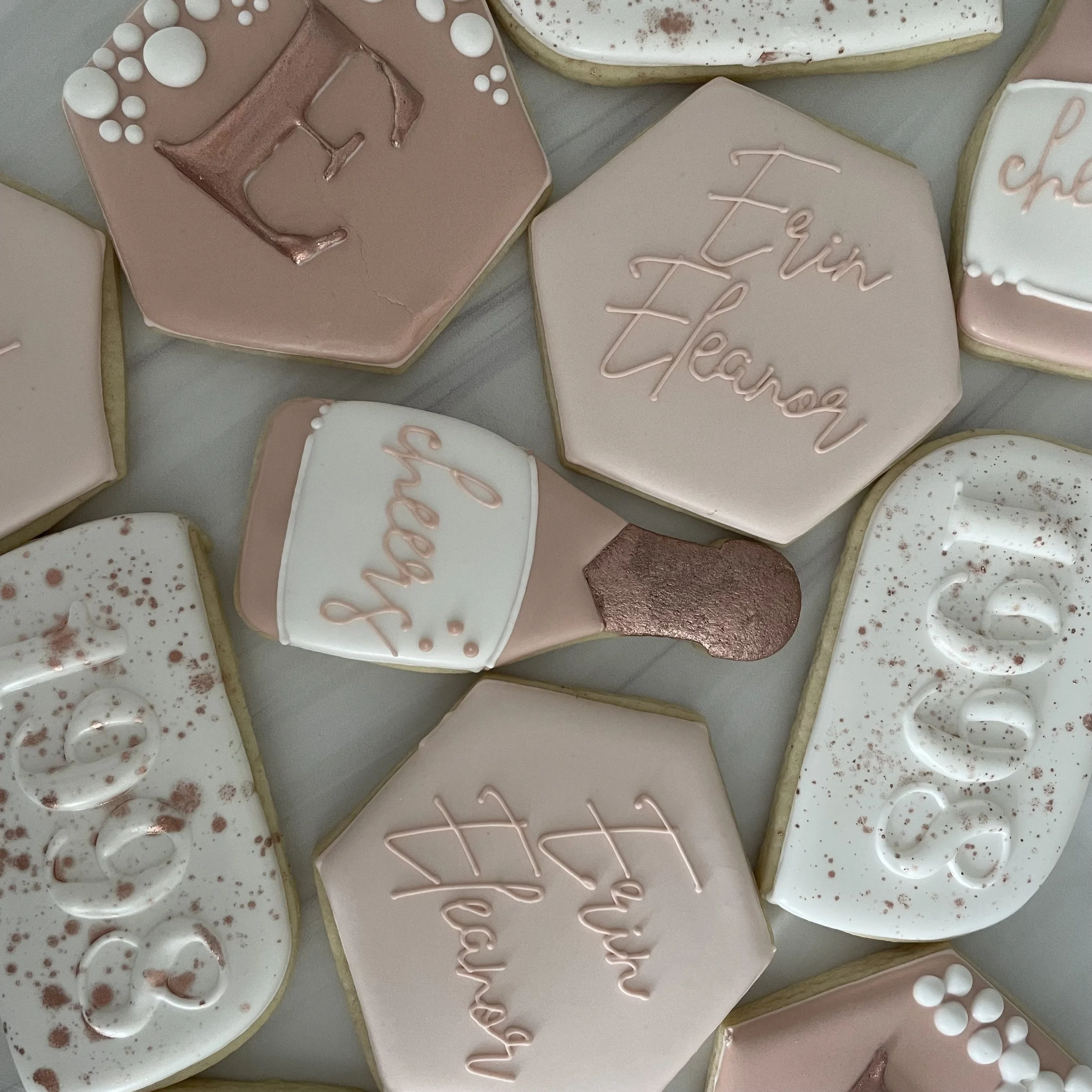 Assorted decorated cookies with pink, white, and speckled designs, some featuring handwritten messages.