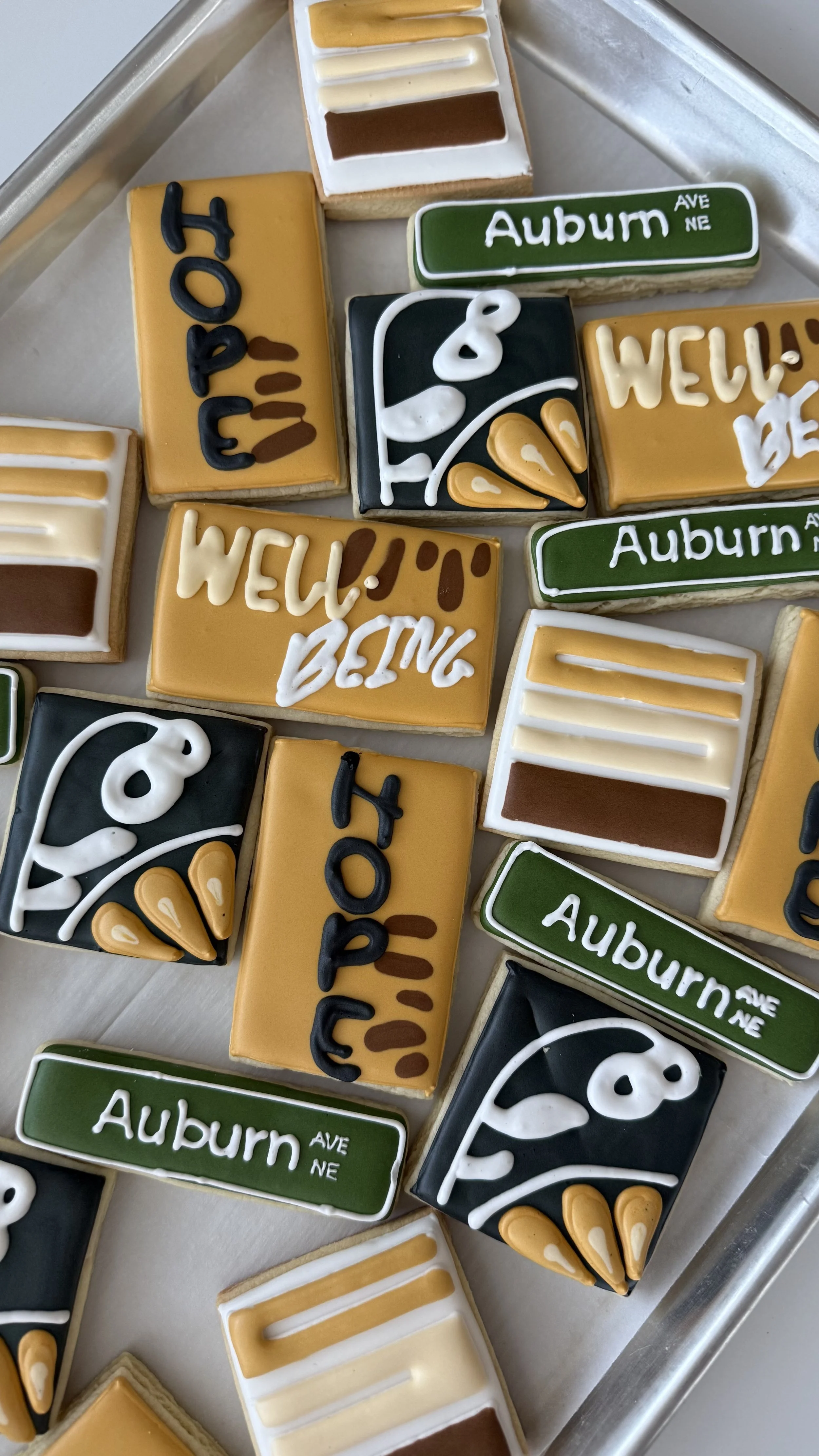 Decorated cookies with various designs, including street signs reading 'Auburn Ave NE', and cookies with stylized labels and patterns featuring black, white, yellow, and green icing.