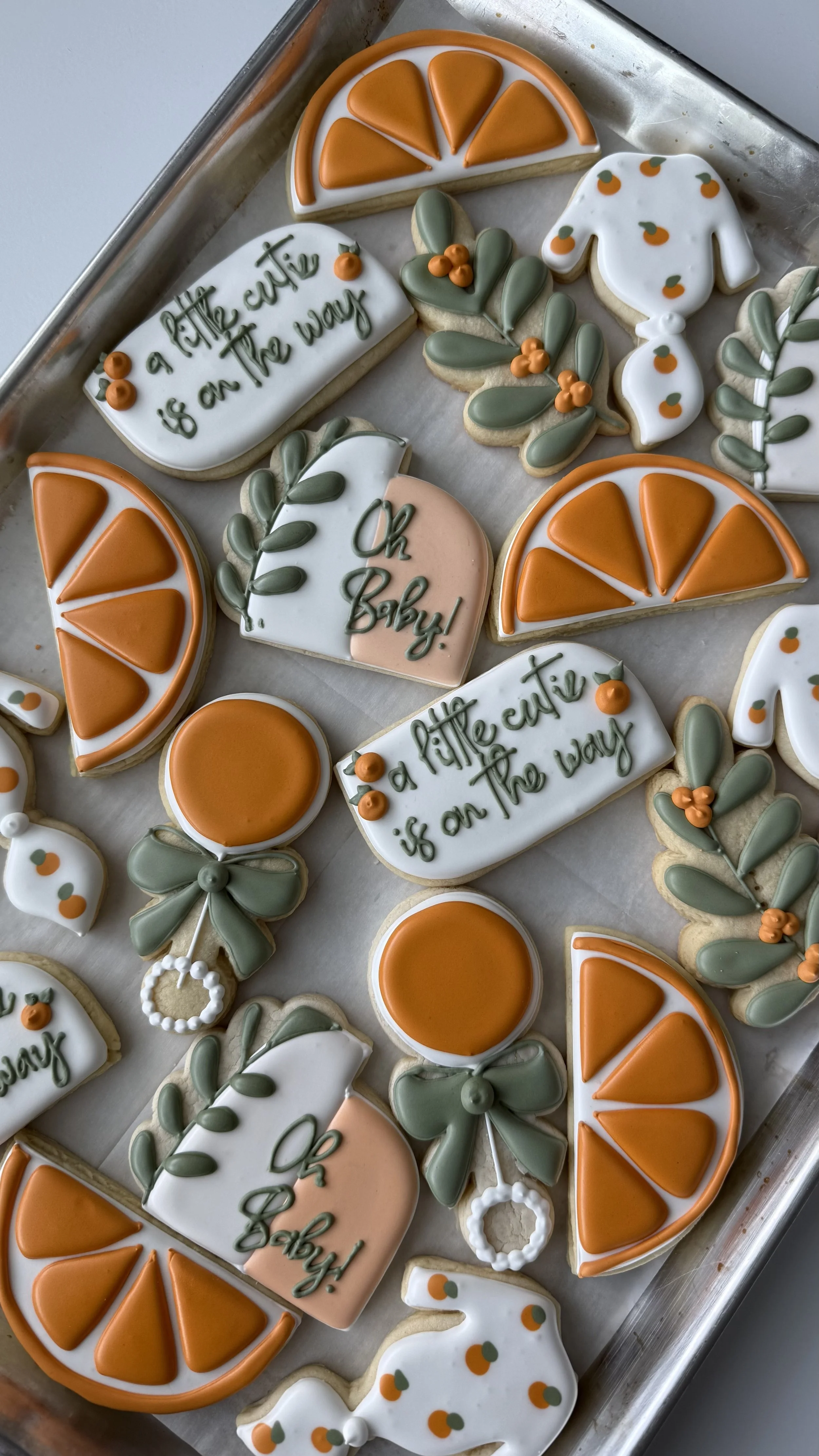Decorated cookies on a tray with orange slices, leaves, and baby themed messages for a gender reveal party.
