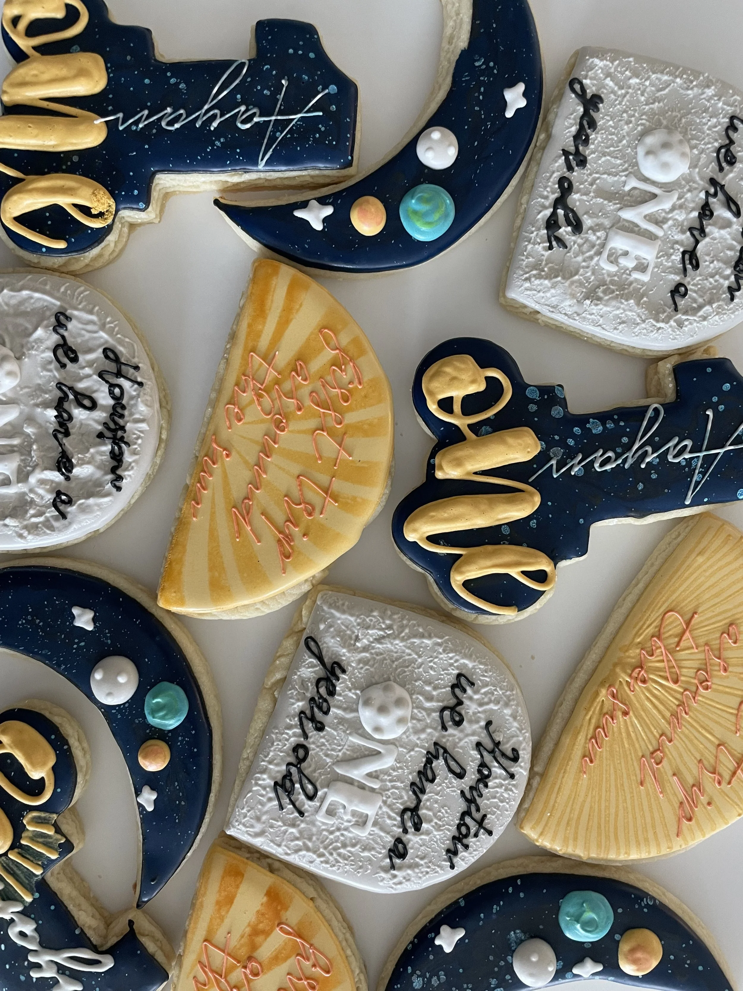 Decorated cookies with space and moon theme, featuring planets, stars, and handwritten messages.