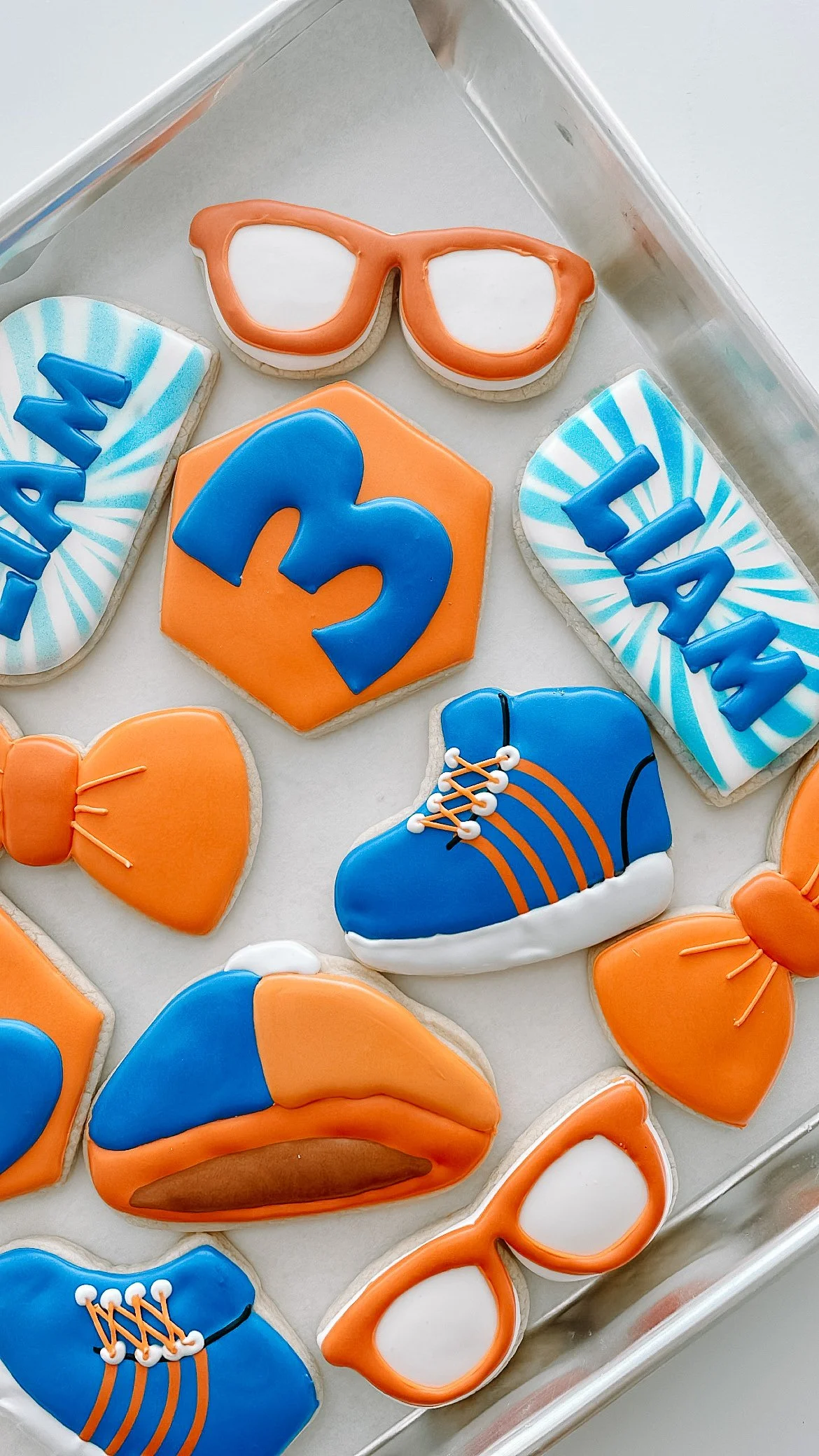 Decorated cookies with a sports theme, including sunglasses, a '3' number, sneakers, and sunglasses, in blue, orange, and white colors.