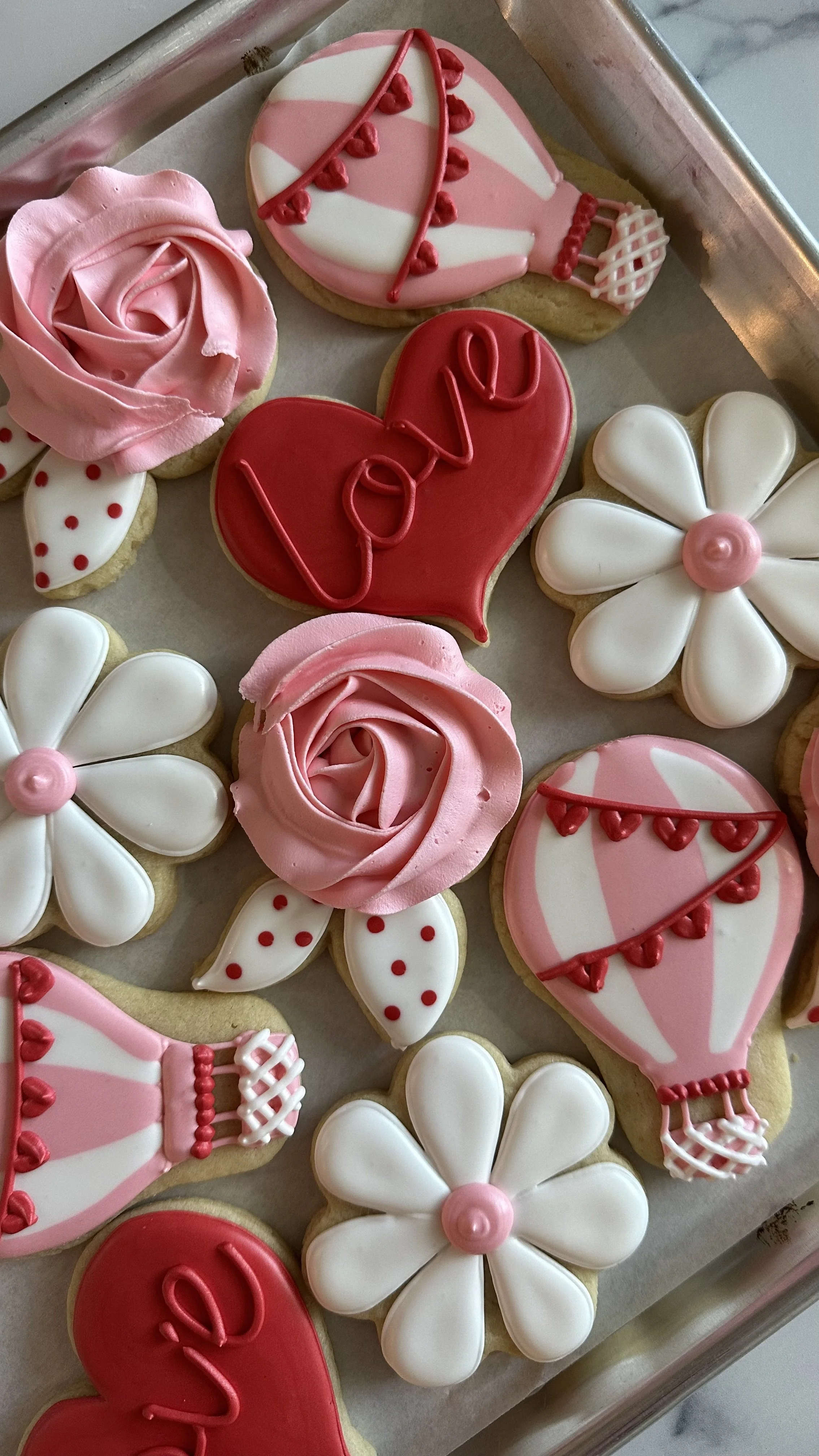 Valentine's Day themed decorated cookies including pink roses, white flowers, hearts with "love" written, and love-themed designs in red, pink, and white icing.