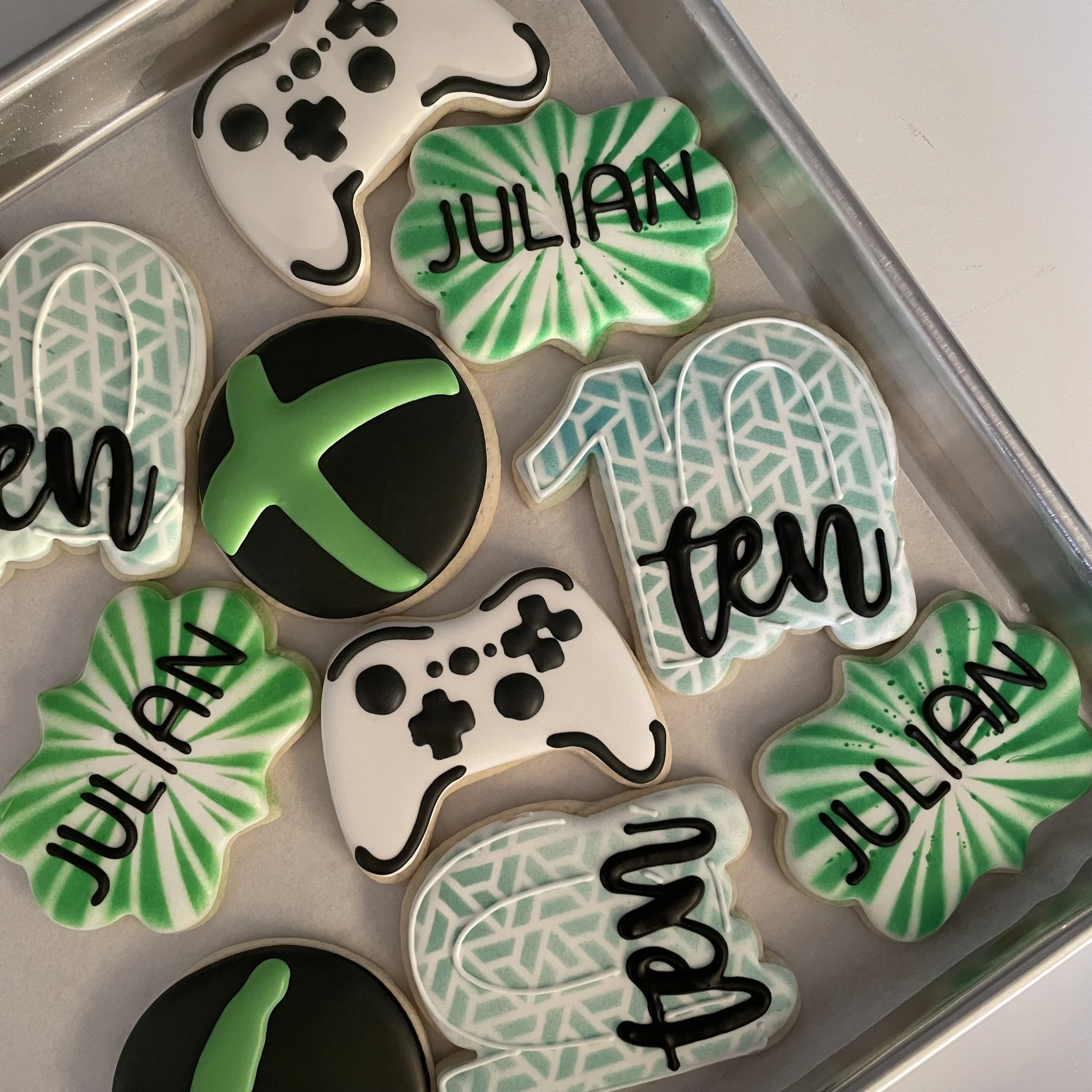 Decorated Halloween cookies with black, white, and green colors, some with the word "Julieann" written on them, arranged on a tray.