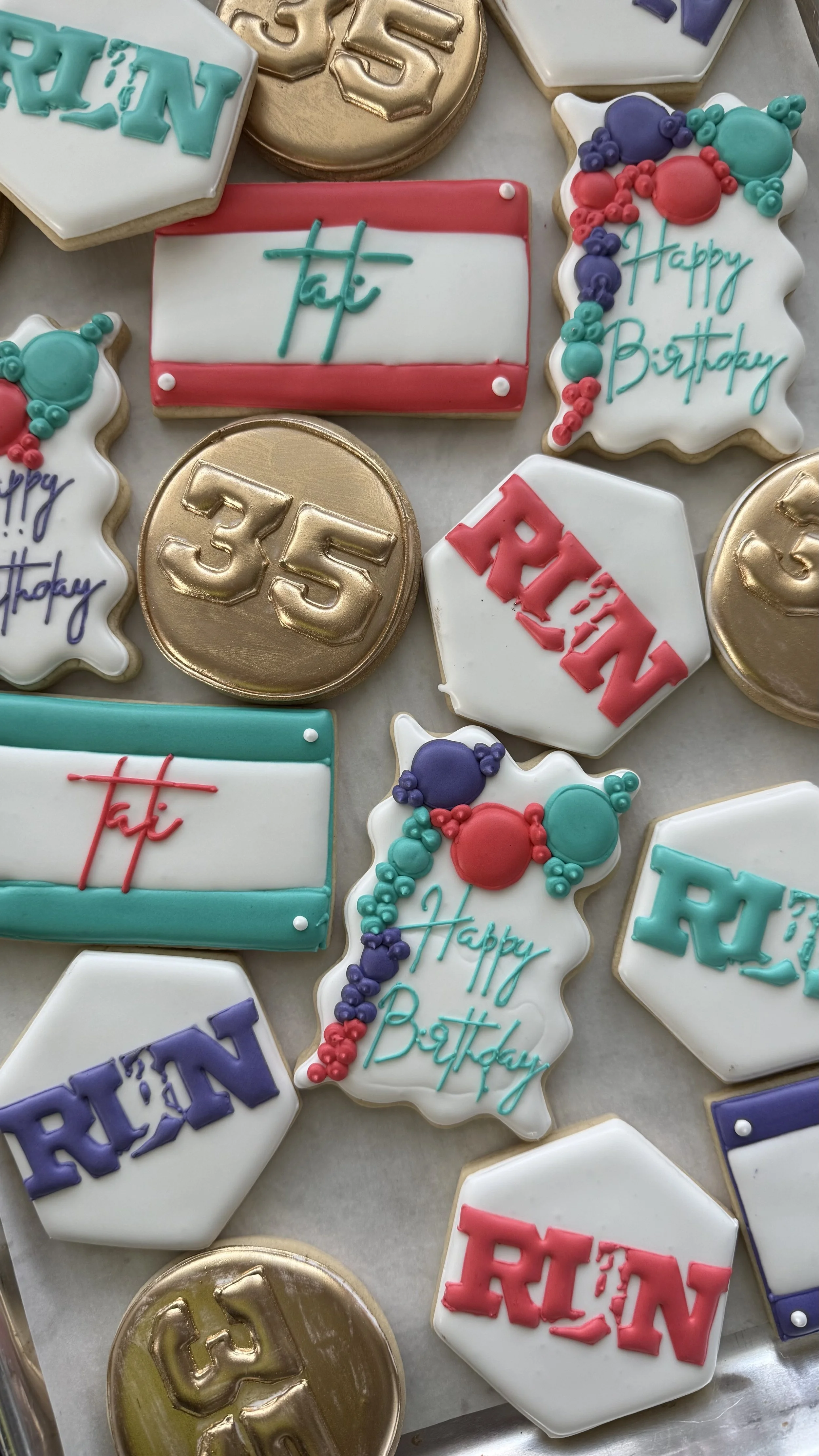 Decorative birthday cookies with various designs including balloons, text, and anniversary numbers, alongside gold and chocolate coins.