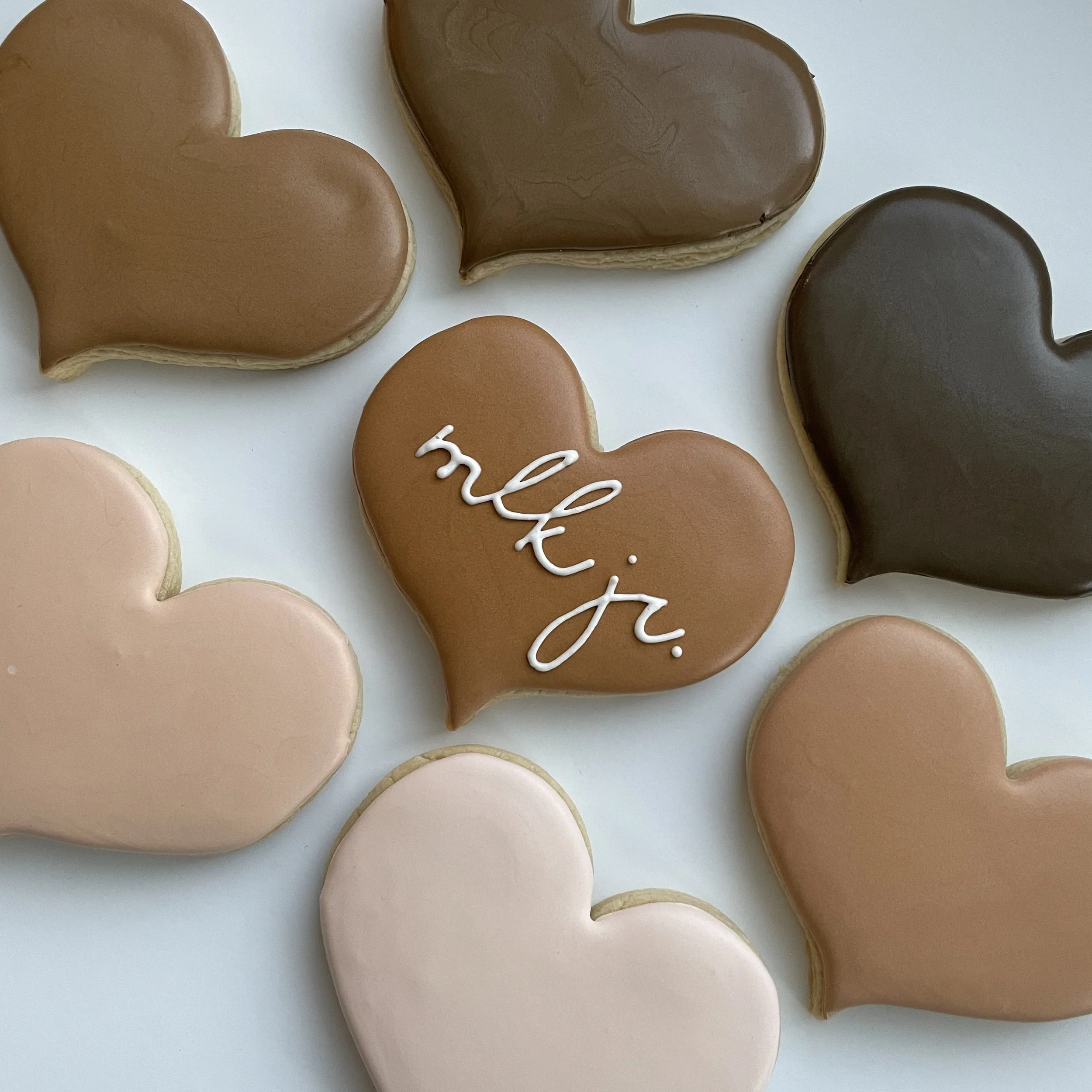 Heart-shaped cookies with chocolate and brown icing, with some white writing on the cookies, on a white surface.
