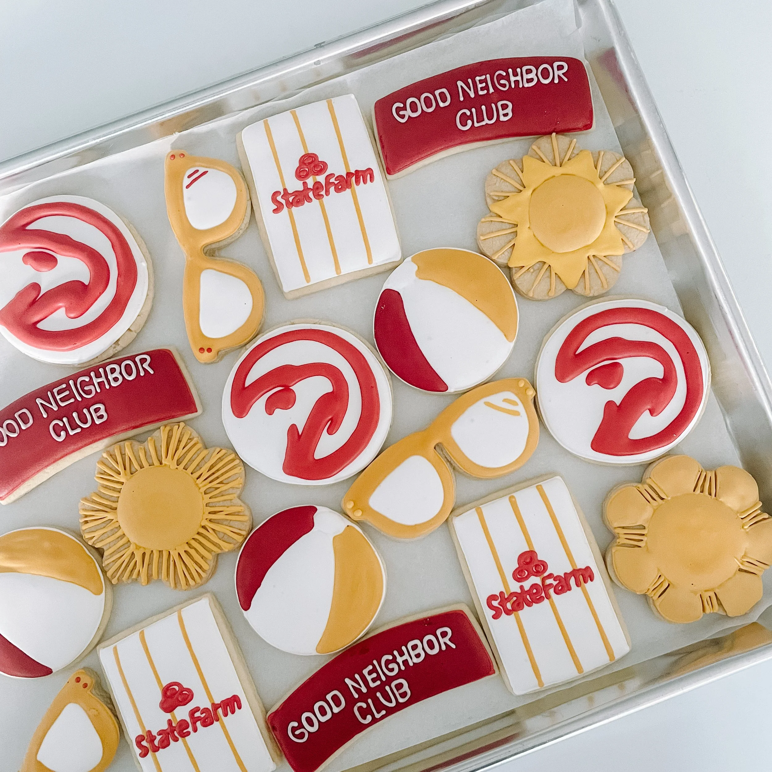 Collection of cookies with various designs including smiles, a mug with 'State Farm' written on it, a red 'Good Neighbor Club' sign, a sunflower, and other shapes decorated with red, yellow, and white icing.