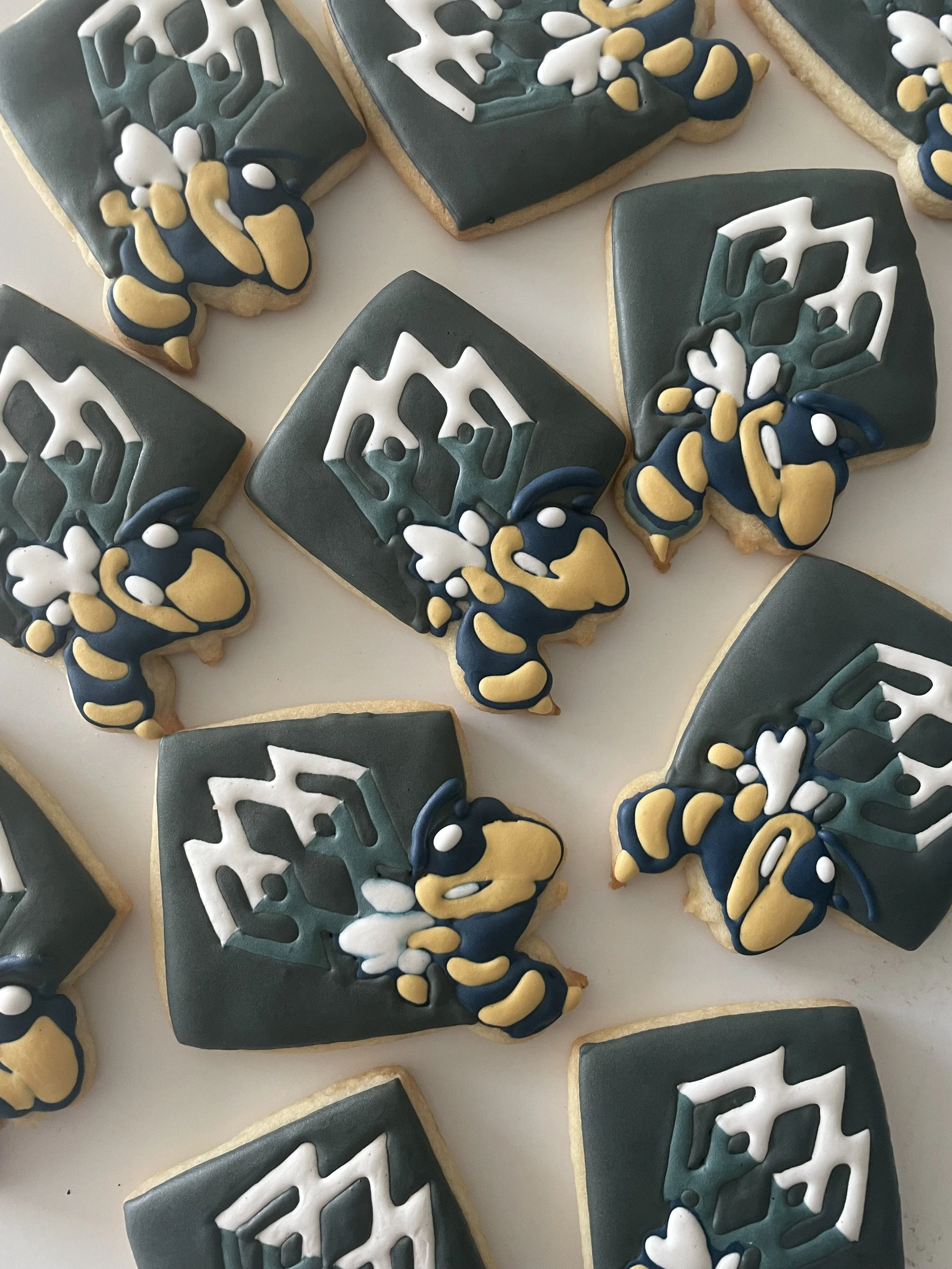 Decorative cookies with dark blue, white, yellow, and teal icing, arranged on a flat surface, featuring geometric and floral patterns.