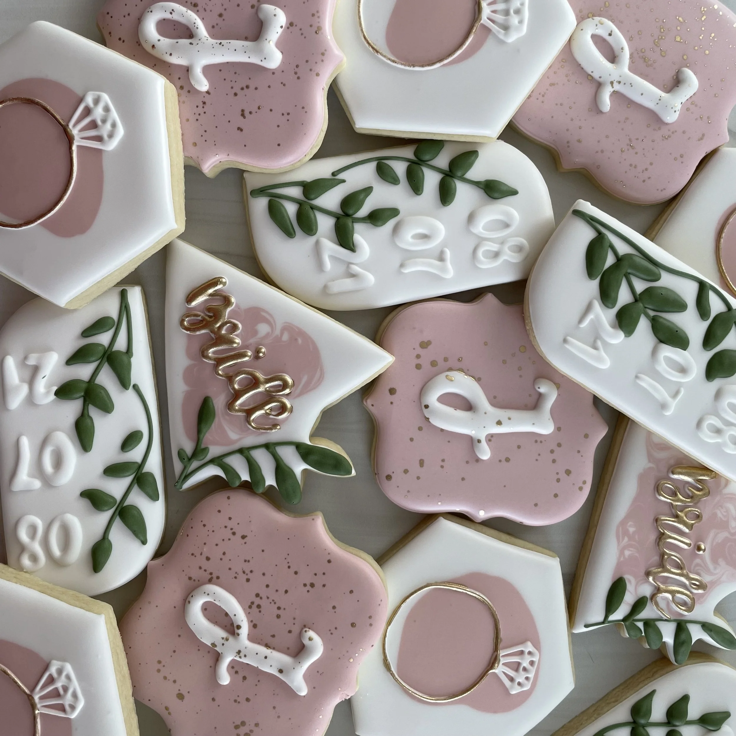 Assorted decorated cookies with pink and white icing, green leaves, and gold accents.