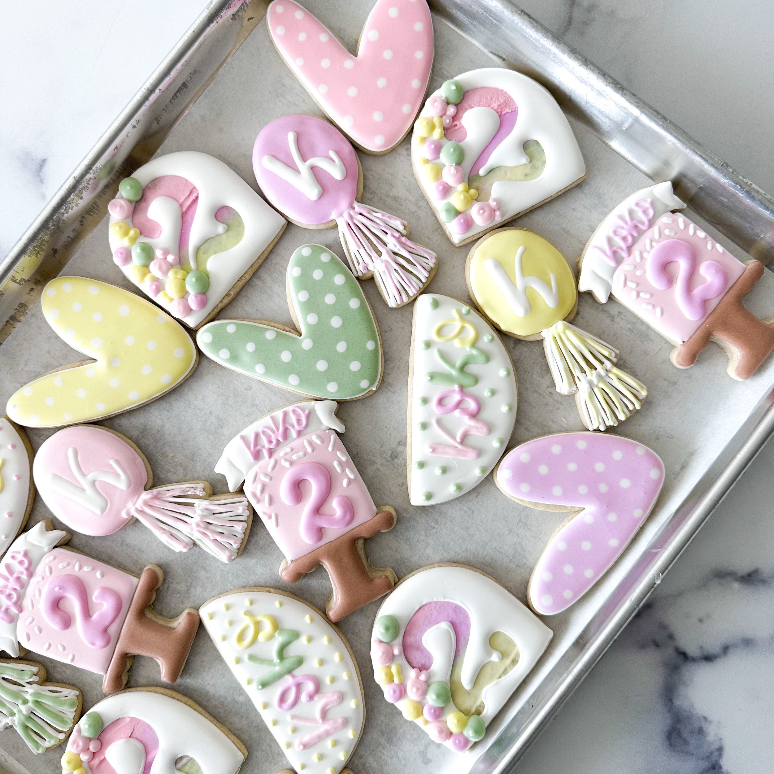 Decorated cookies on a tray, including hearts, Easter eggs, and bunny shaped cookies with pink, white, yellow, and green icing.