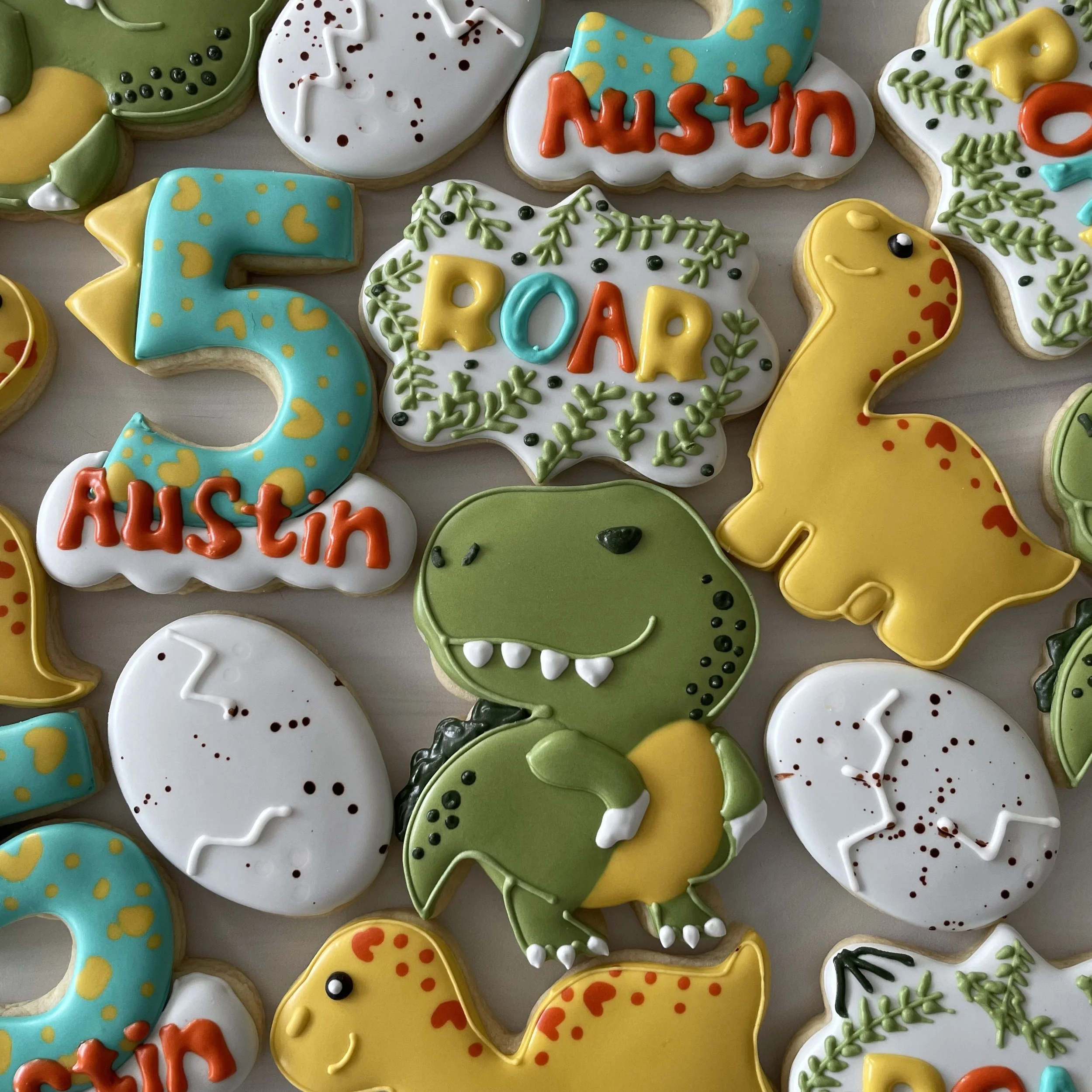 A collection of decorated cookies in various shapes, including animals, numbers, and names, with colorful icing and sprinkles, celebrating a birthday with the name 'Austin' and age '5'.