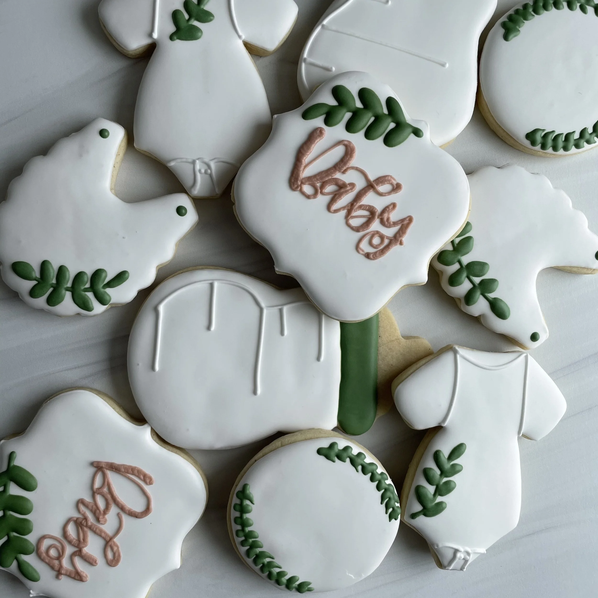 Decorated sugar cookies with white icing, green leafy designs, and some with pink script writing.