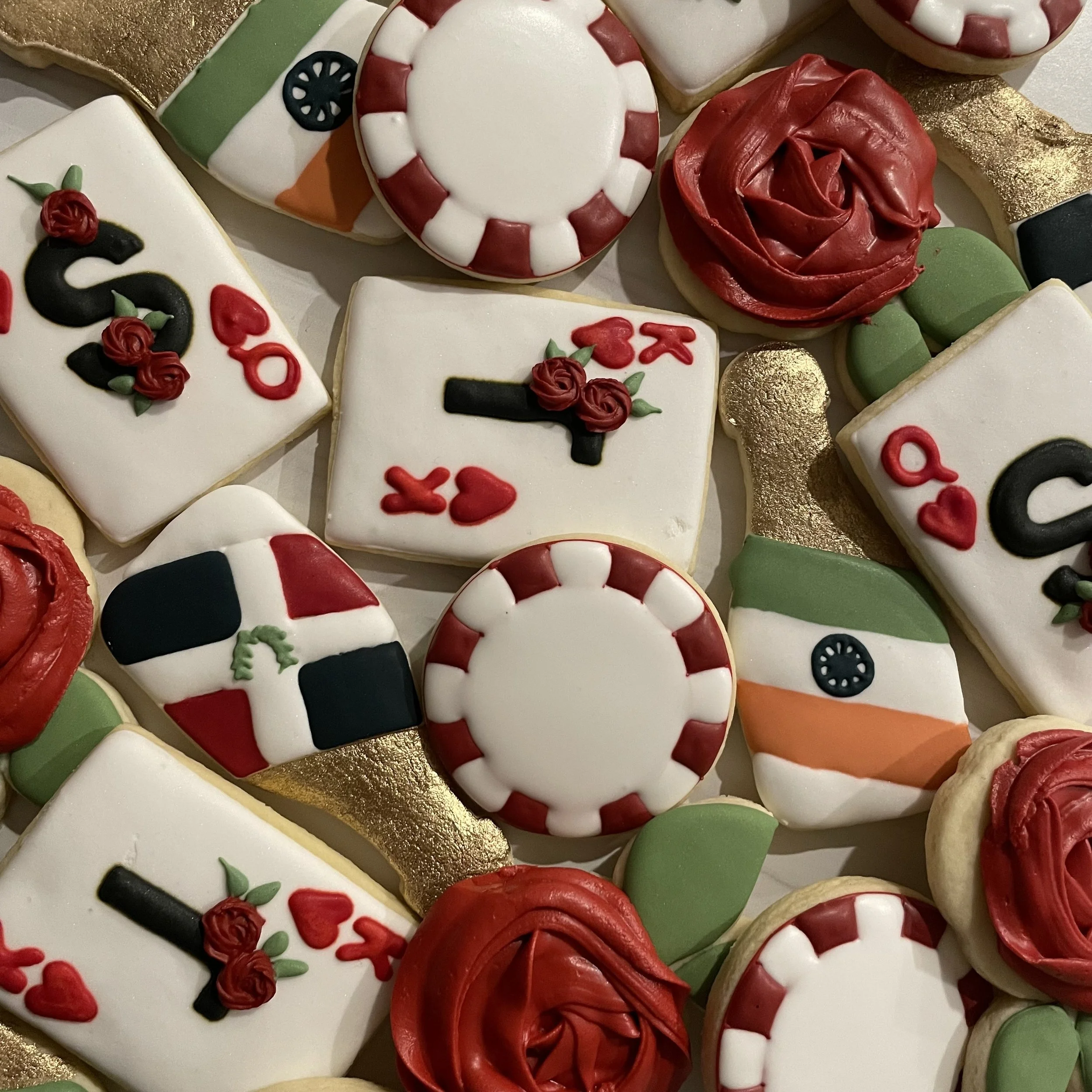 Assorted decorated sugar cookies for Christmas, including a candy cane, a Christmas wreath, and other holiday-themed shapes with red, green, white, and gold icing.