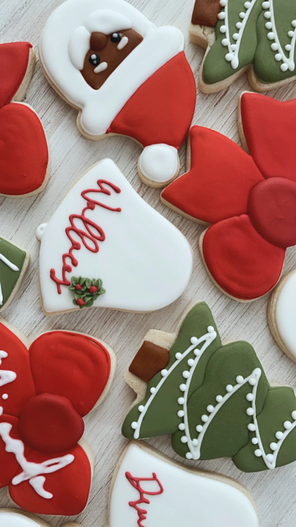 Decorated cookies with Christmas themes, including a Santa face, holly, a Christmas tree, and a white heart with a red 'Merry' message.