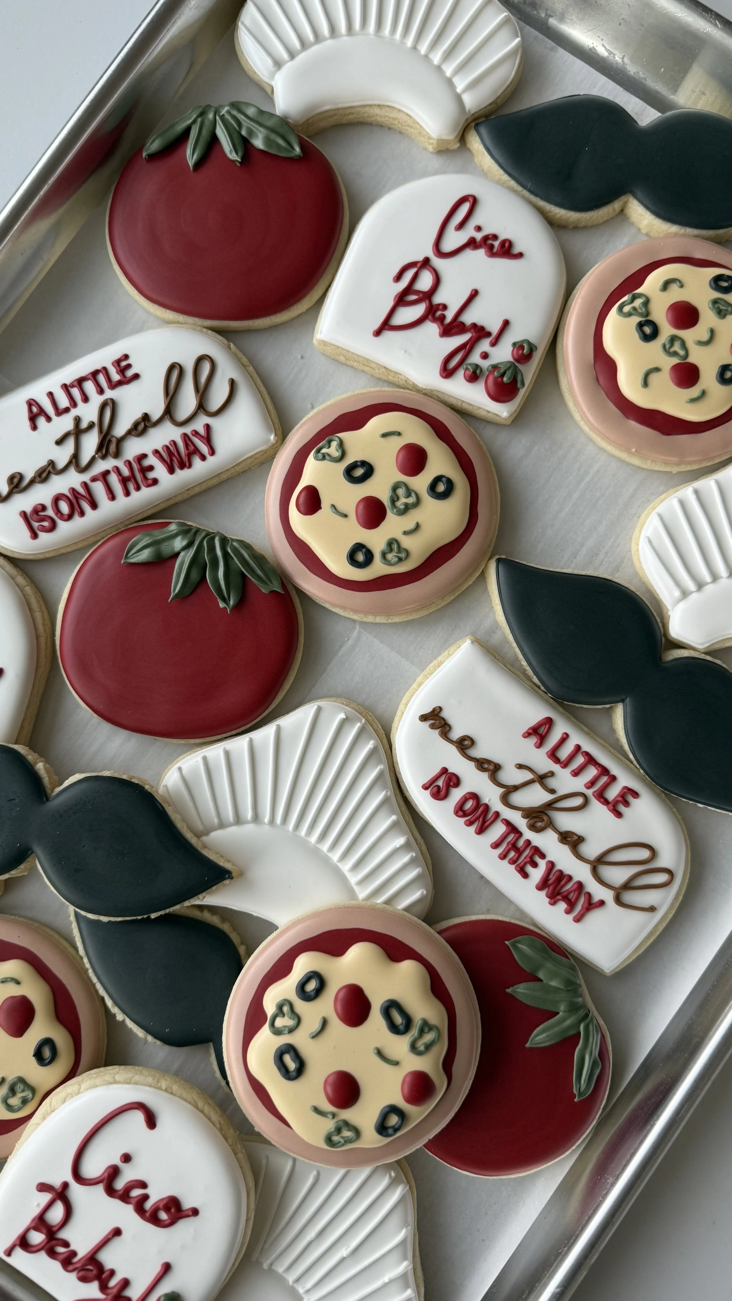 Decorative cookies with pizza and tomato themes, some with messages like 'Cici Baby!', 'ALLTIE is on the way', and other food-related designs, arranged on a tray.