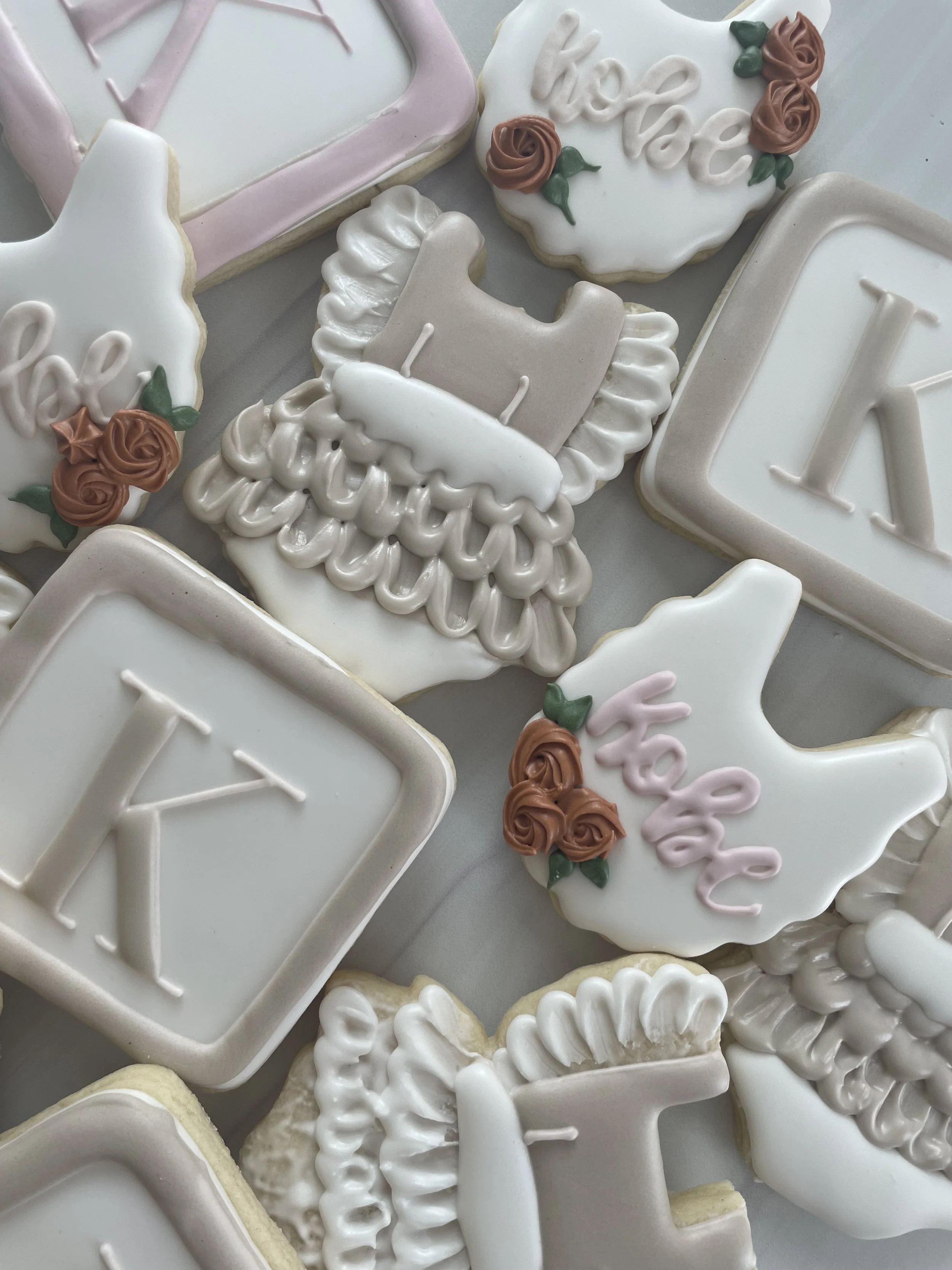 Assorted decorated cookies with white and pink icing, some with words like 'love' and 'xo', featuring floral and geometric designs.