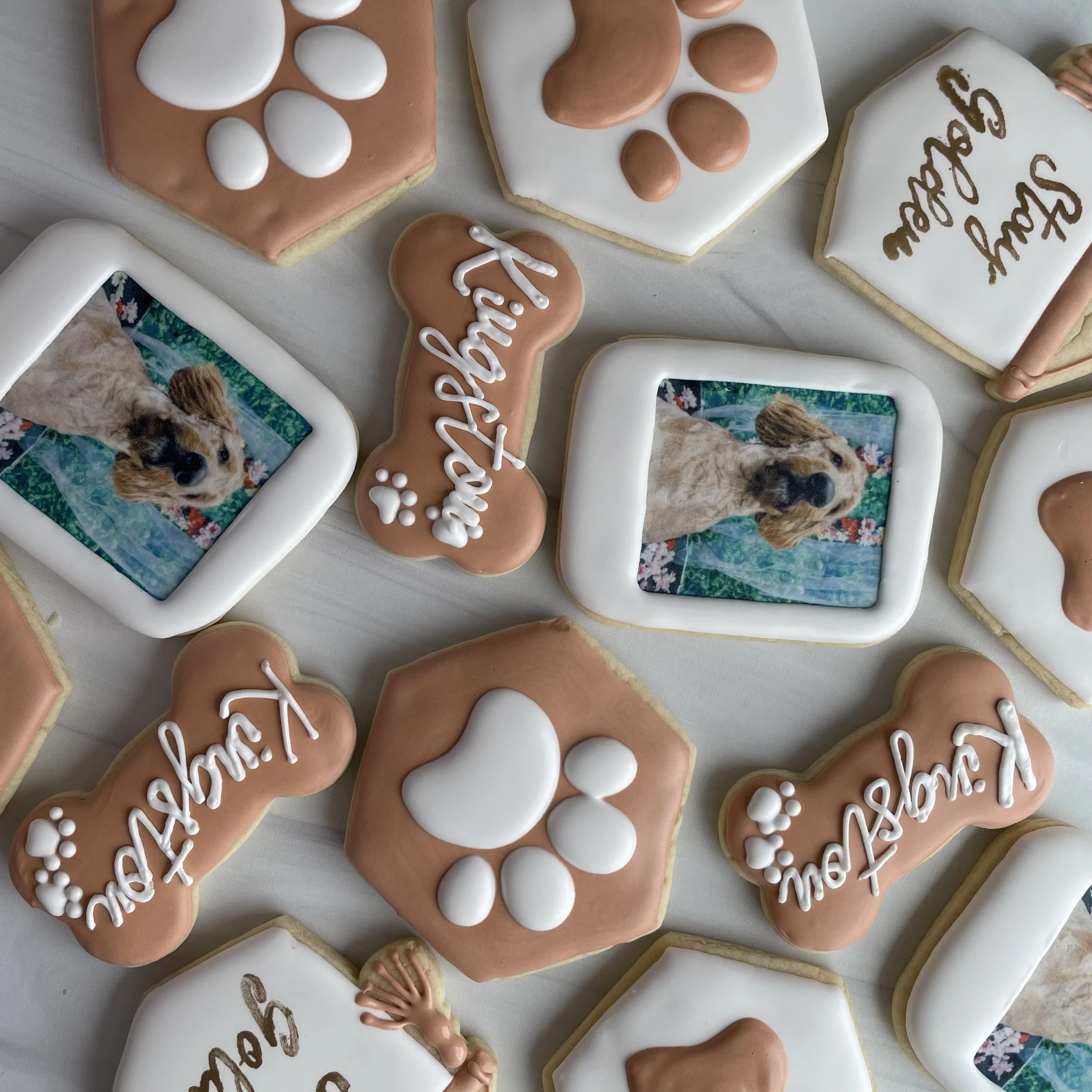 Collection of decorated sugar cookies with paw print and nature photos, some with writing like 'thank you'.