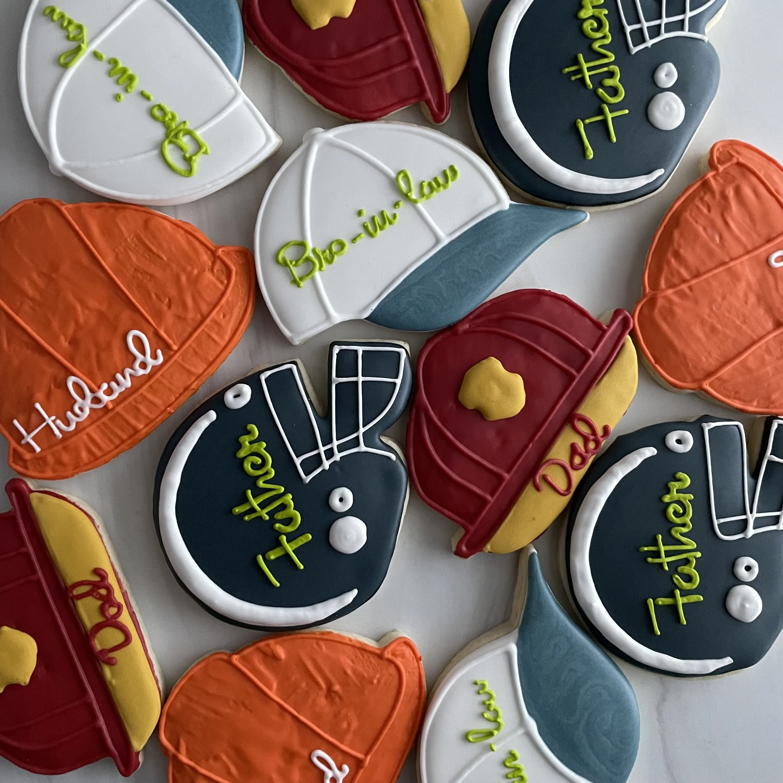 Colorful decorated cookies with sports themes, including football helmets, footballs, and basketballs, with some featuring writing.