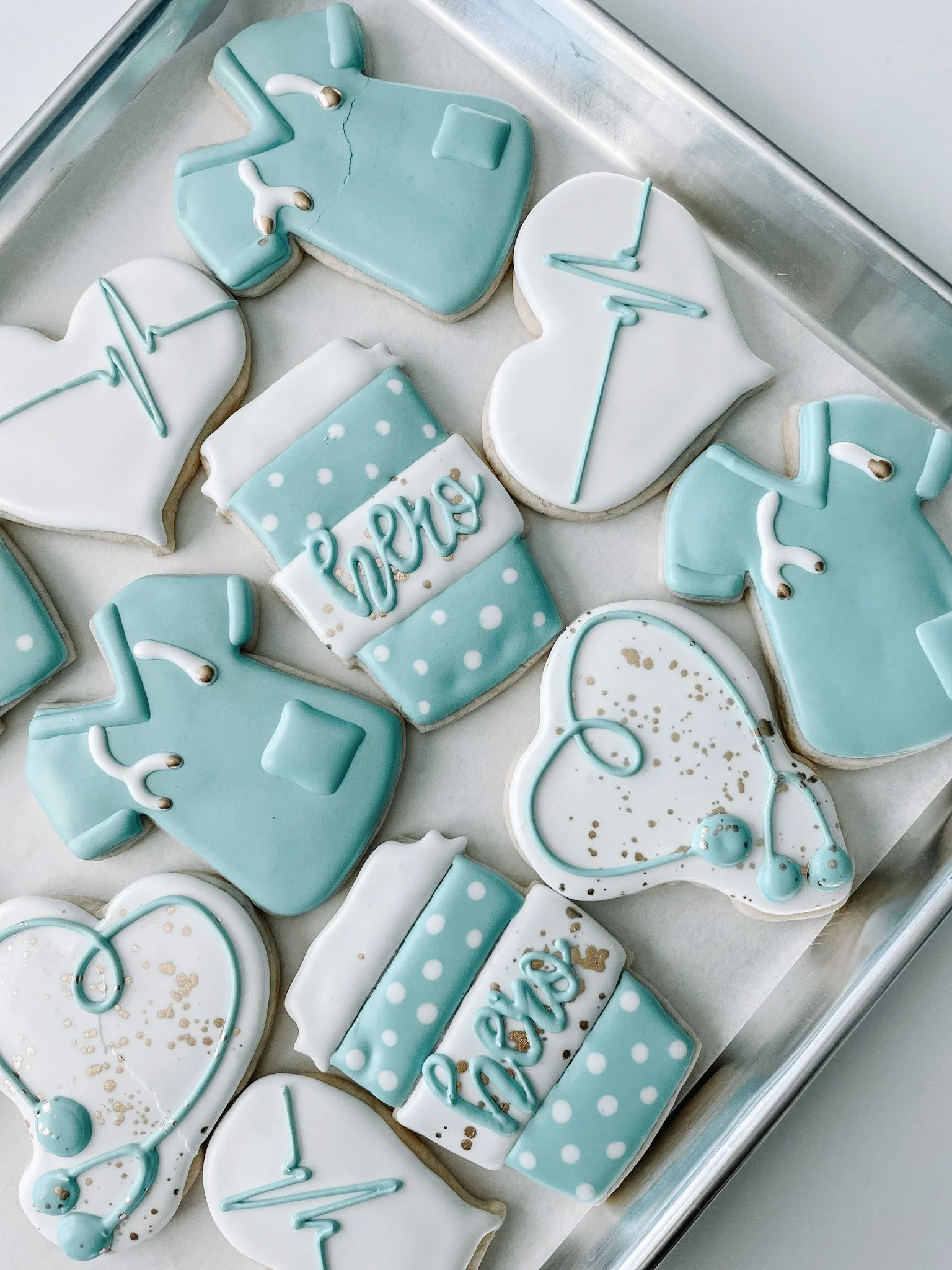 Assorted medical-themed cookies in blue and white with stethoscope and heart shapes, decorated with icing.