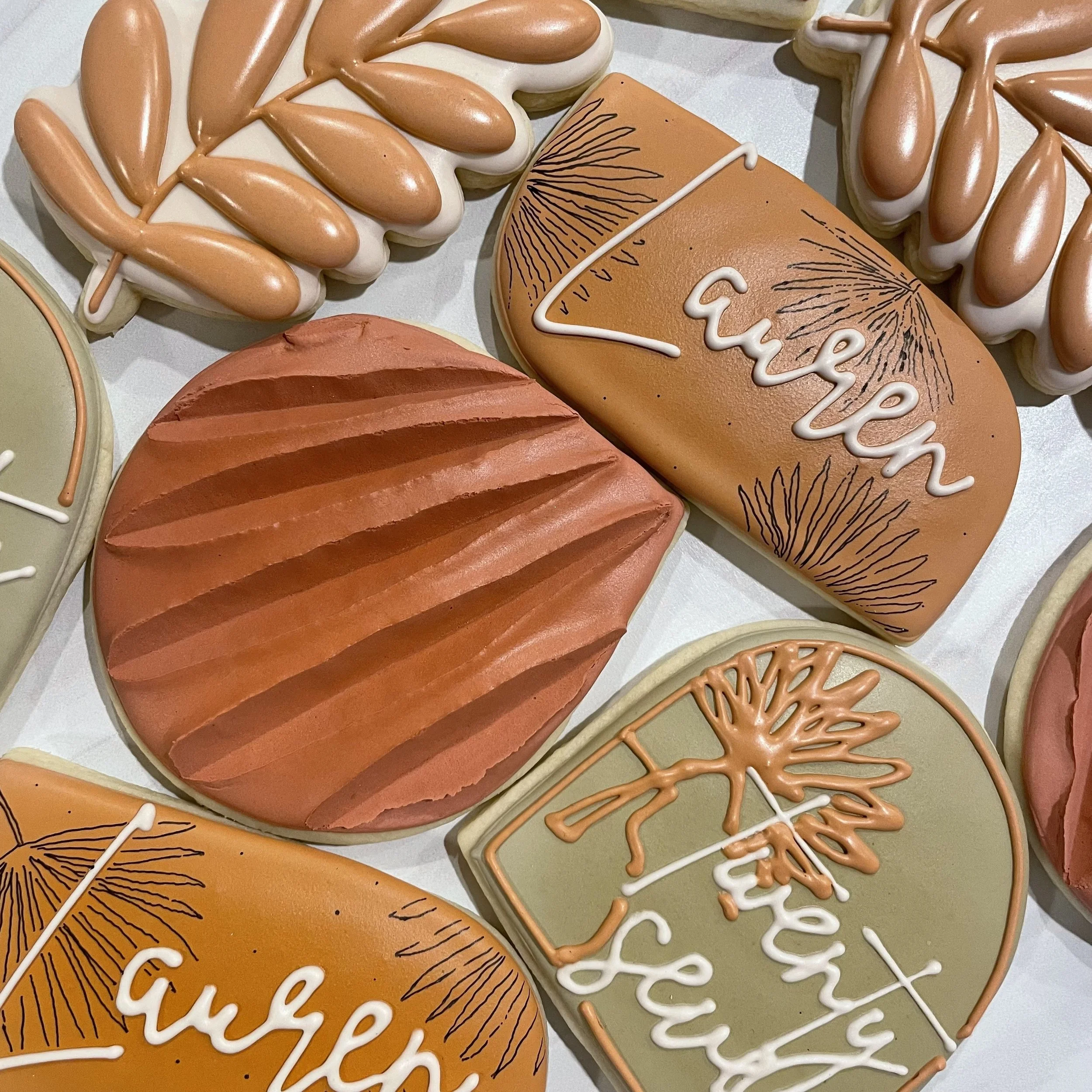 Decorative cookies shaped and decorated with icing, featuring botanical designs and the words "Love" and "Gather" in cursive.