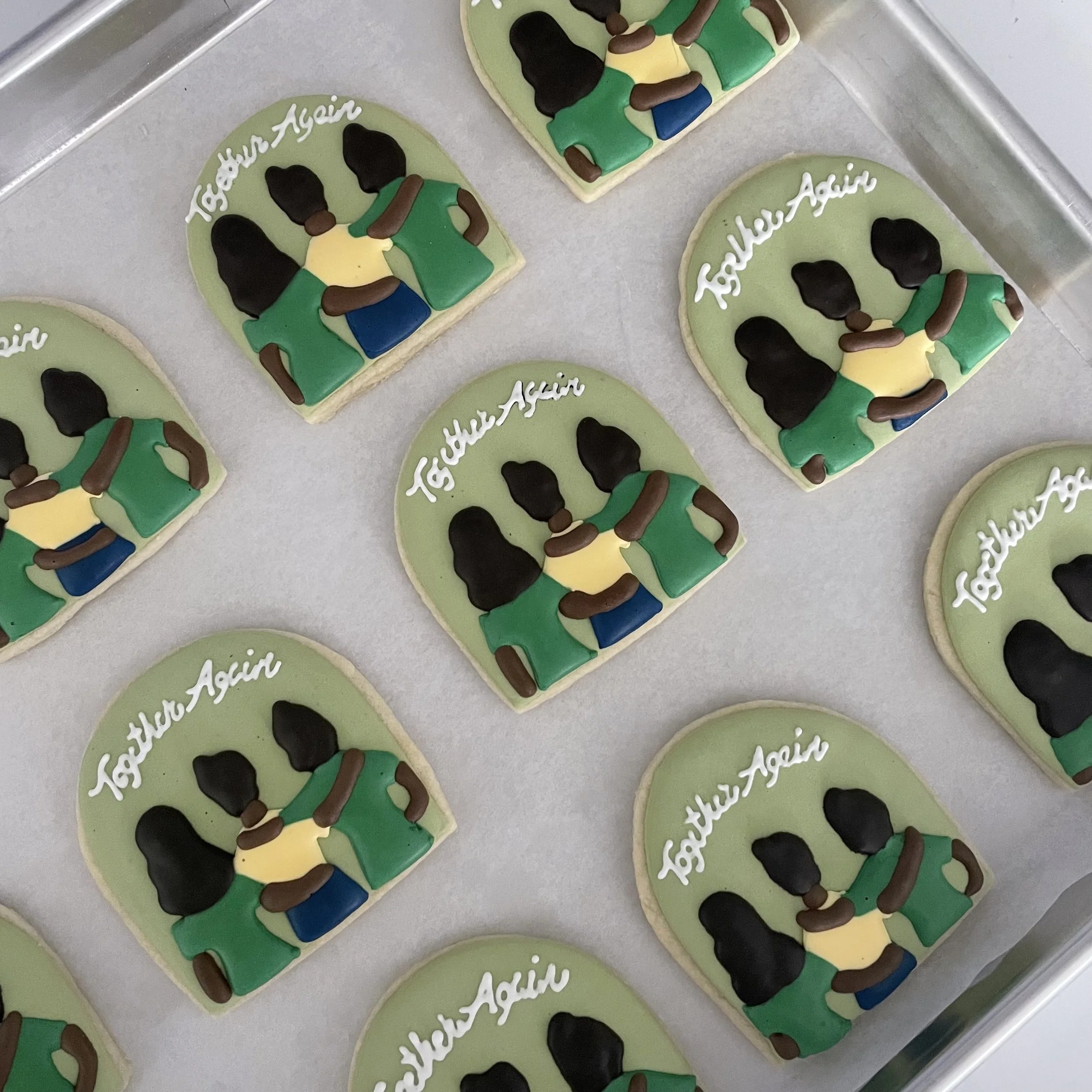 Decorative cookies with green icing, black hair, yellow shirts, green shorts, and blue shoes, with white text reading 'Thank You Again' on each cookie, placed on a silver tray.