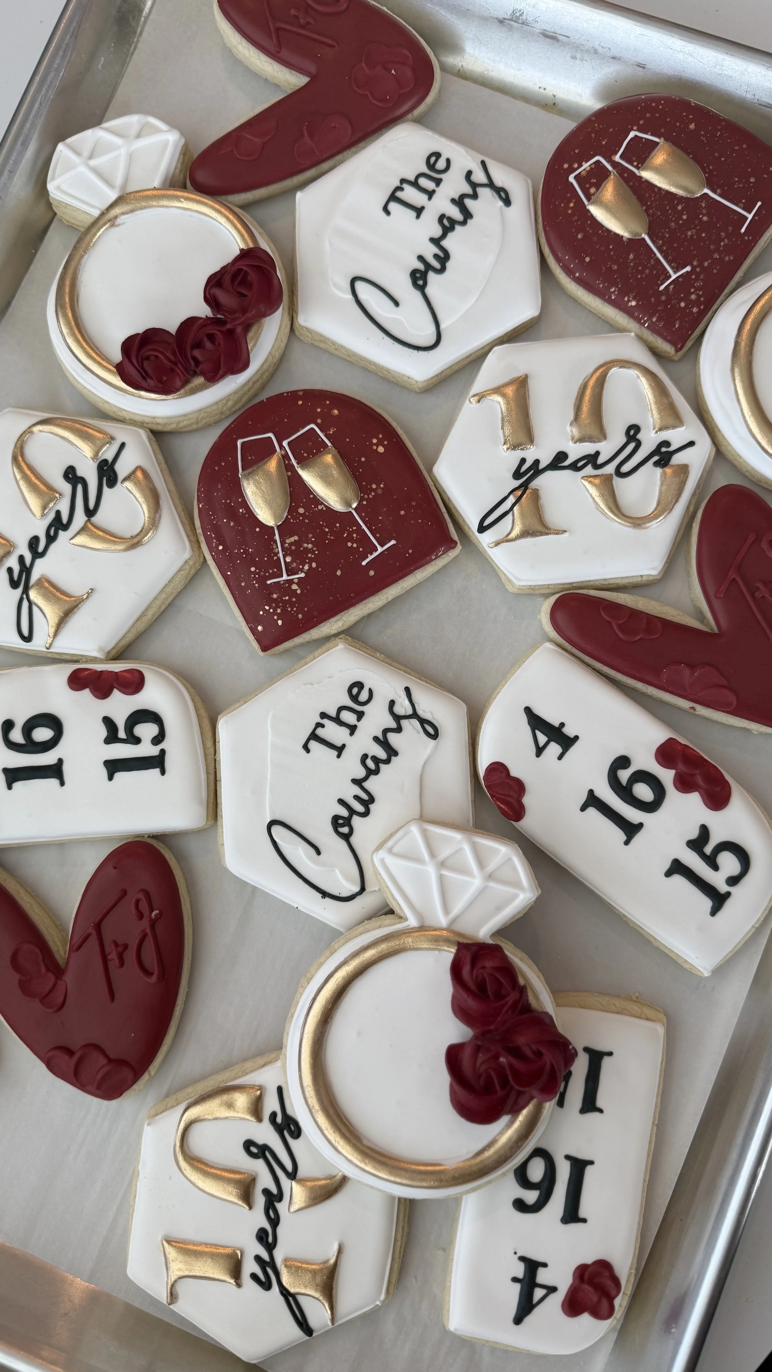 Assorted decorated cookies celebrating a 16th birthday and a graduation. The cookies feature phrases like "The Queen," "16 & fabulous," and "10 years." They are decorated with gold, red, white, and black icing, with some cookies featuring champagne g