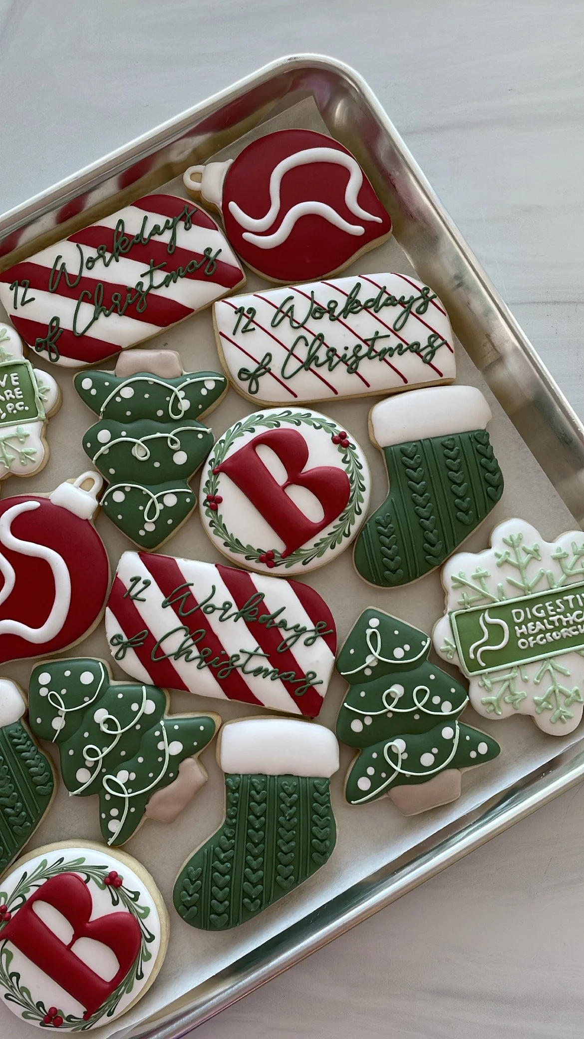 Christmas-themed decorated cookies on a tray, including ornaments, a mitten, a Christmas tree, and a cookie with the message "12 W0rkdays of Christmas."