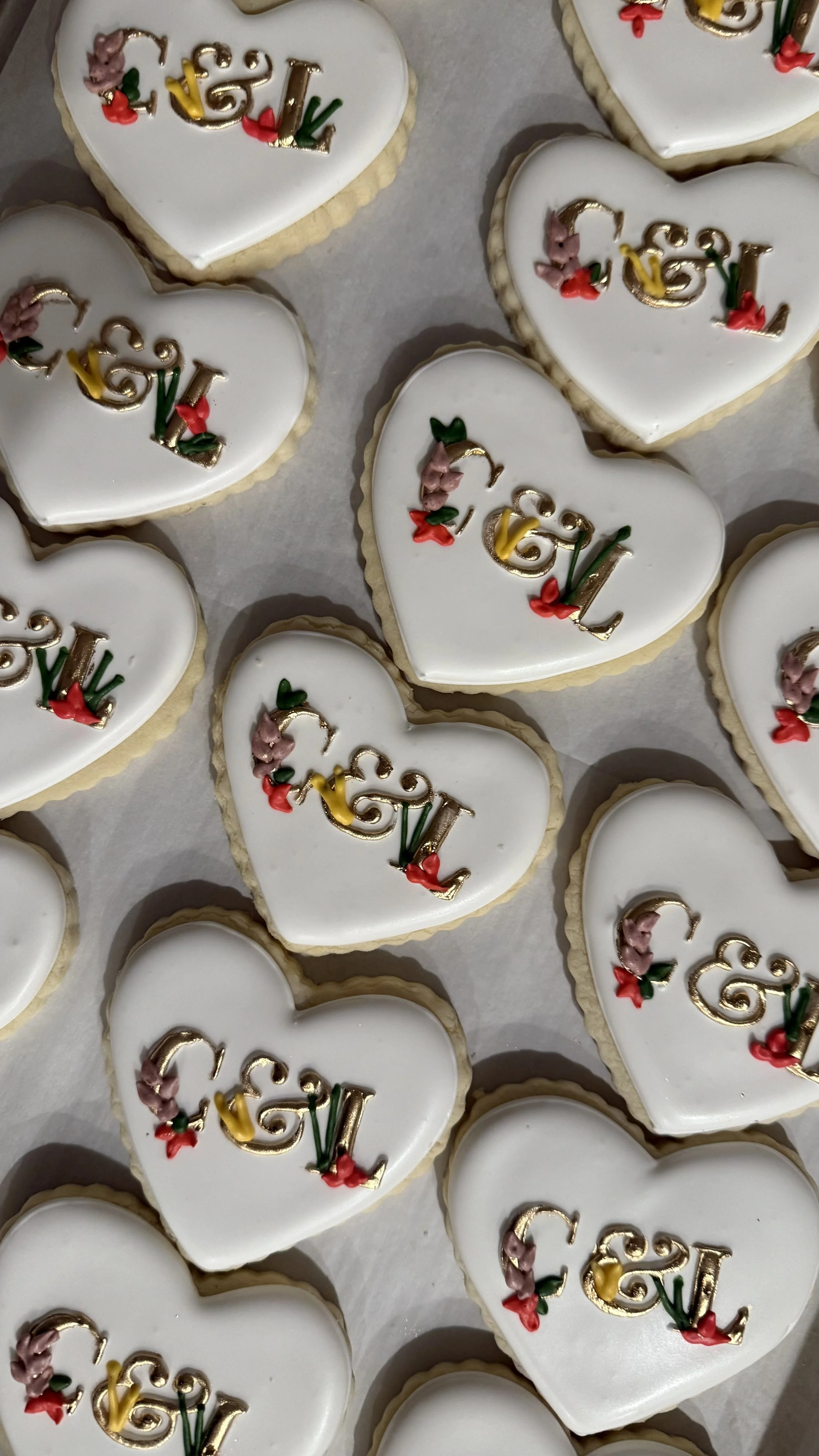 Heart-shaped cookies with white icing, decorated with the word "GAY" in colorful letters and floral accents.