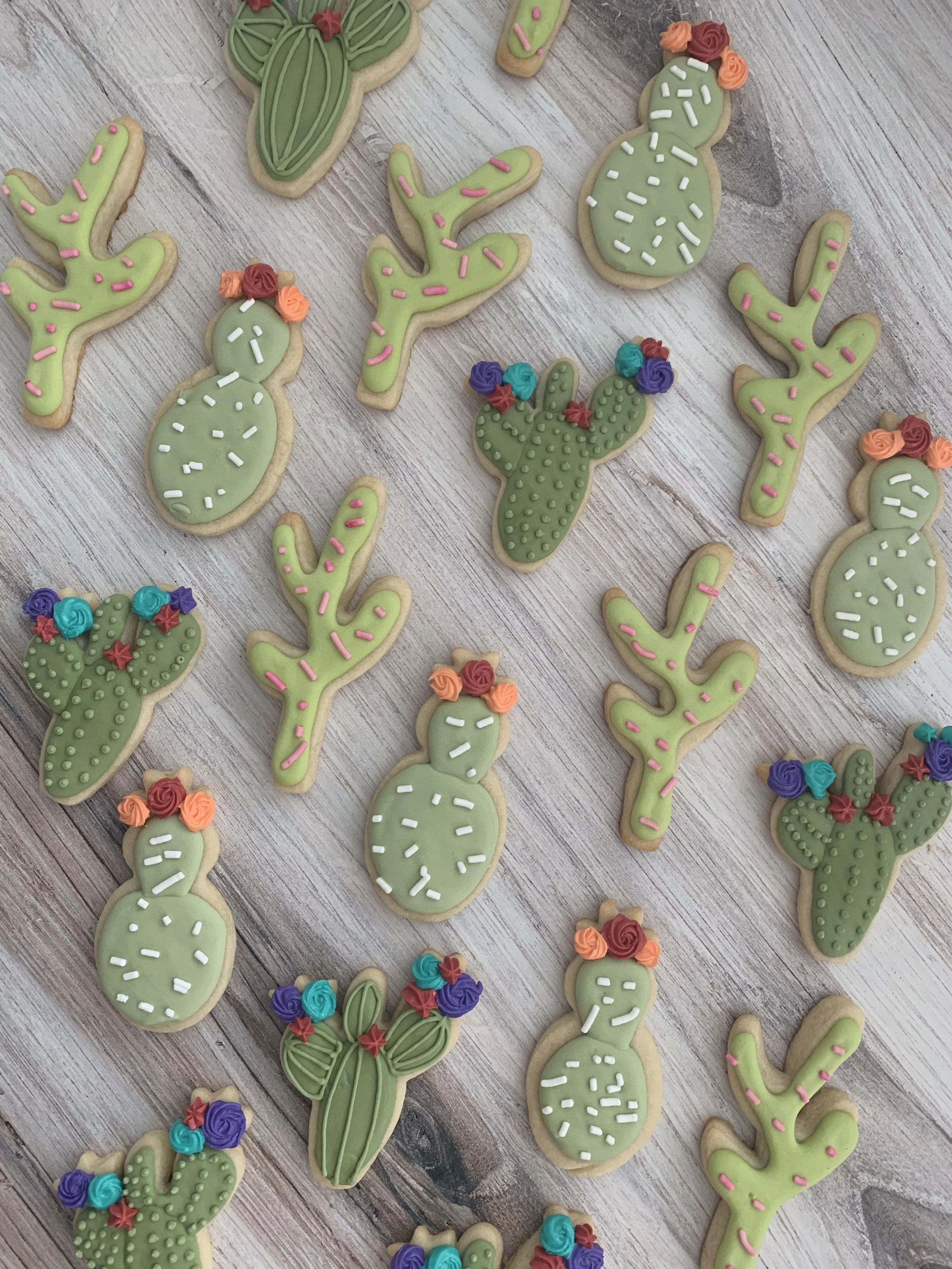 Cookies iced to resemble various cactus plants, decorated with colorful frosting flowers on a wooden surface.