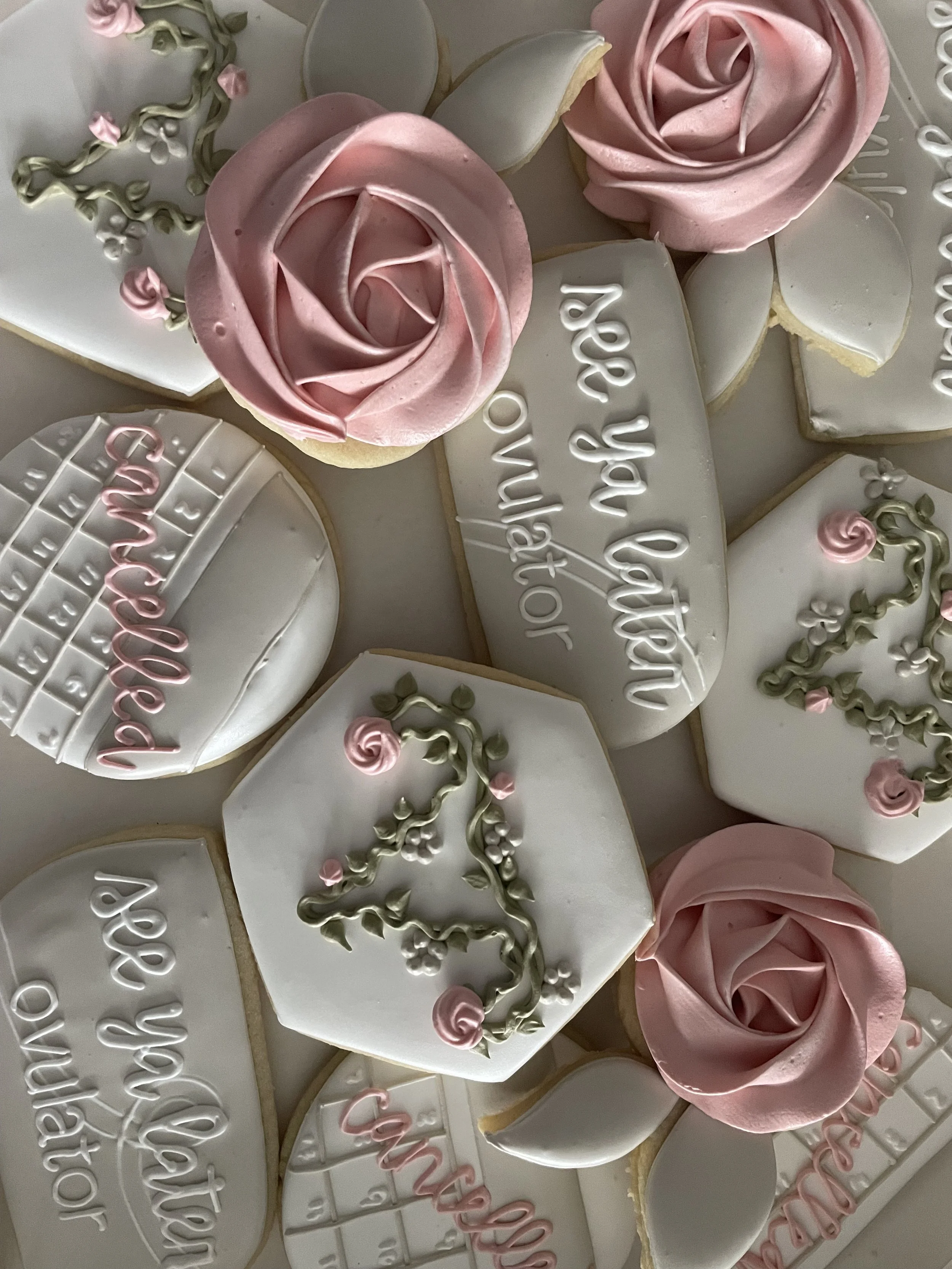 Heart-shaped cookies decorated with white icing, pink l rose-shaped icing, and green icing leaves. Some cookies have messages written in white or pink icing for Mother's Day.