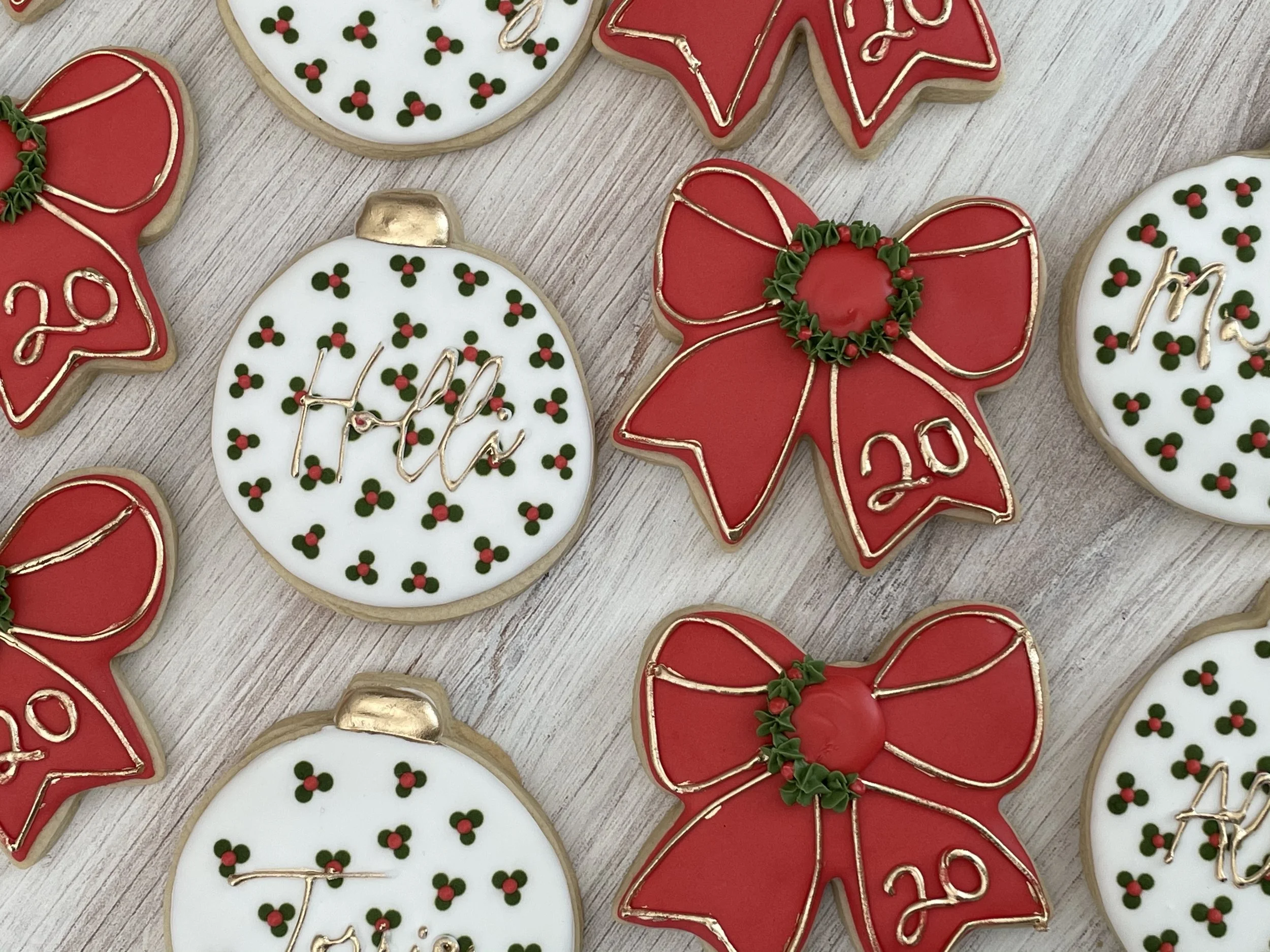 Decorated Christmas cookies with red, white, and green icing in various festive shapes, including a Christmas tree, ornaments, and a bow, on a wooden surface.