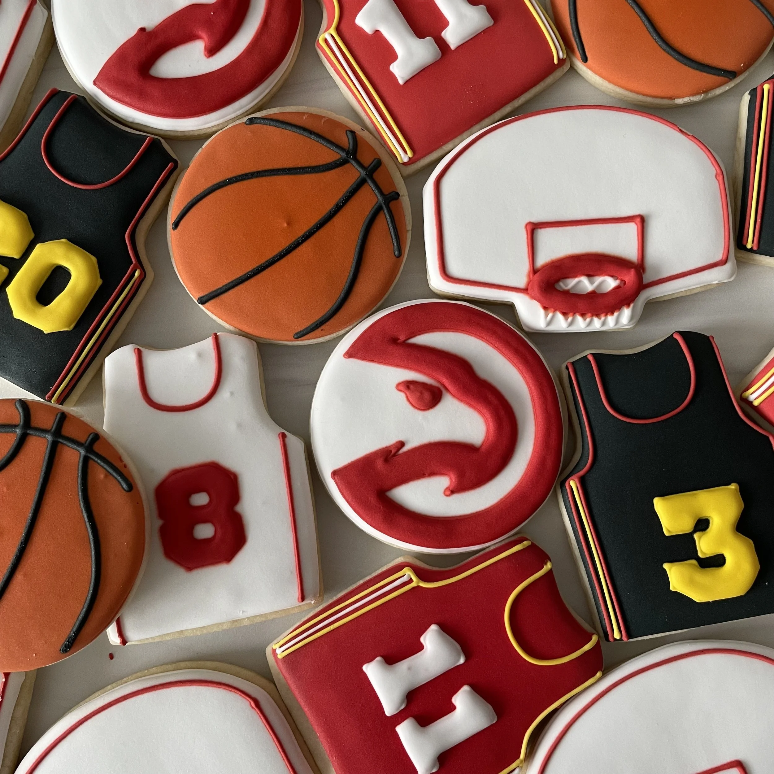 Decorated cookies shaped like basketballs, footballs, and other sports-related items with colorful icing.