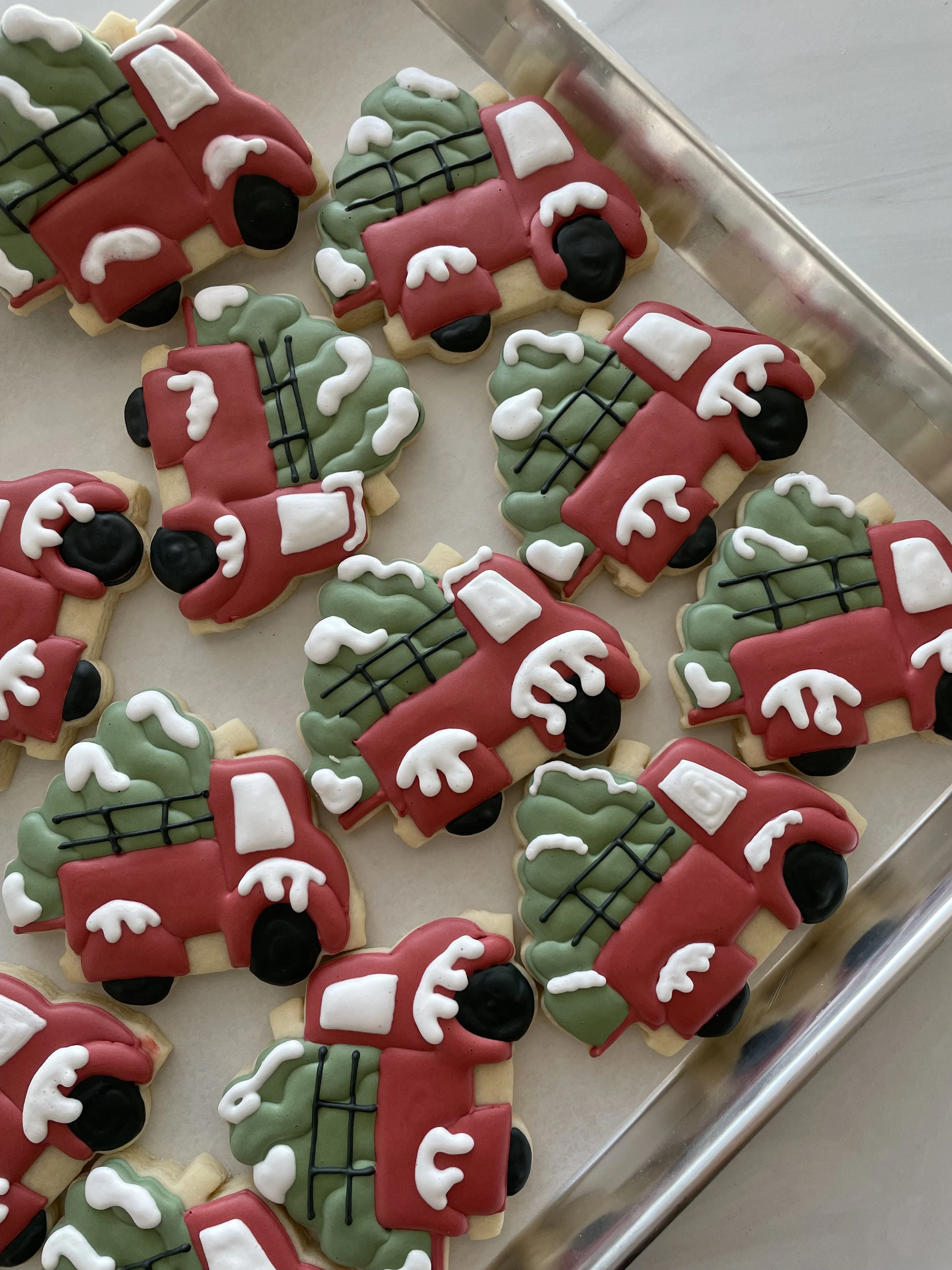 Christmas-themed sugar cookies decorated as toy fire trucks with red bodies, black wheels, green compartments, and white accents.