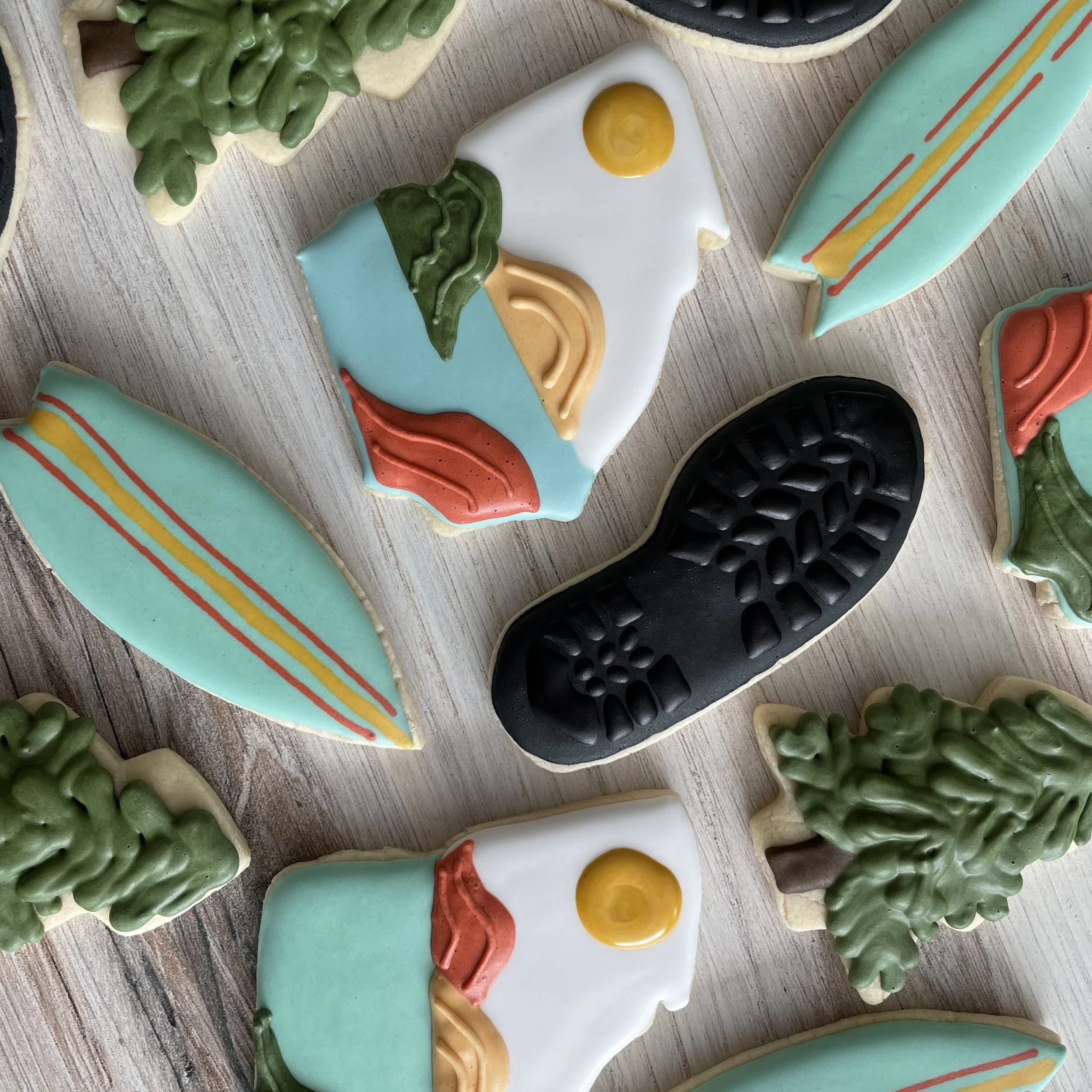 Colorful sugar cookies decorated with icing in shapes of eggs, plants, shoes, and abstract patterns on a wooden surface.