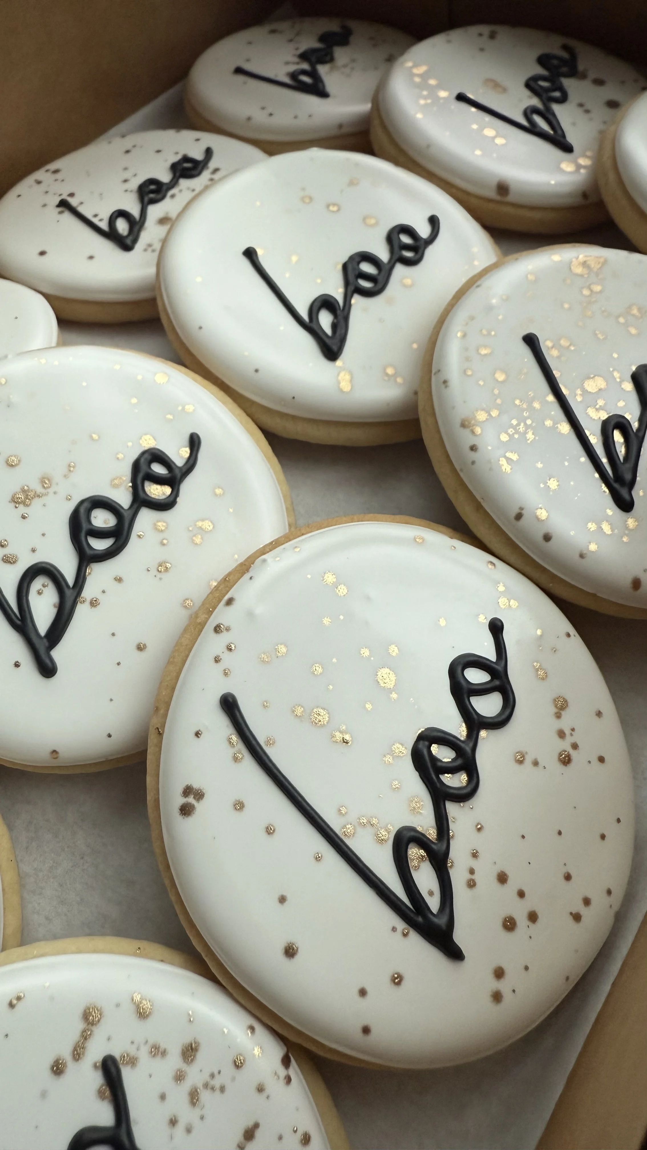 Cookies with white icing, gold and black sprinkles, and the word 'Baby' written in black icing.