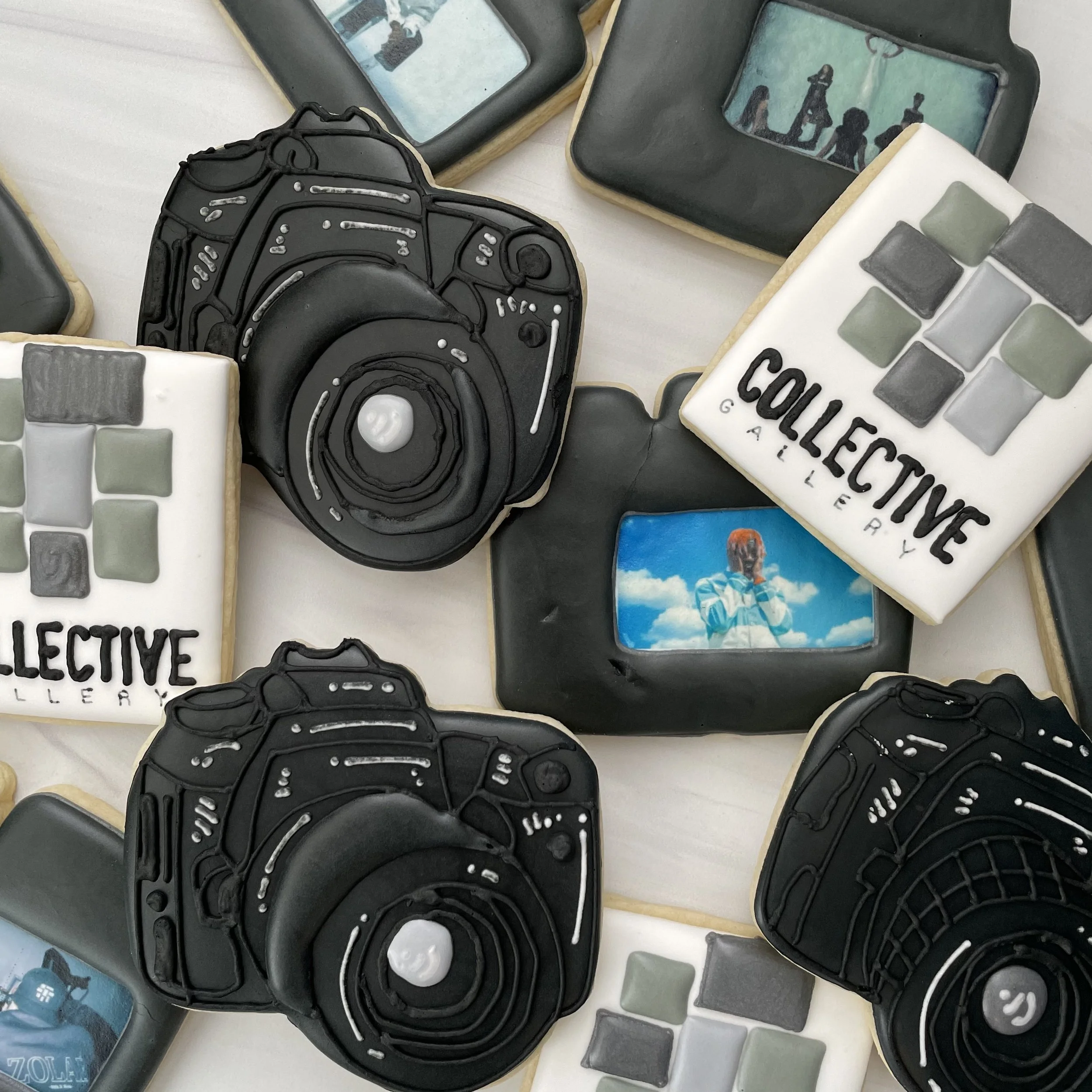Decorated cookies shaped and decorated like a camera, a computer keyboard, and a group of people silhouettes, with some cookies bearing text and others with colored squares.