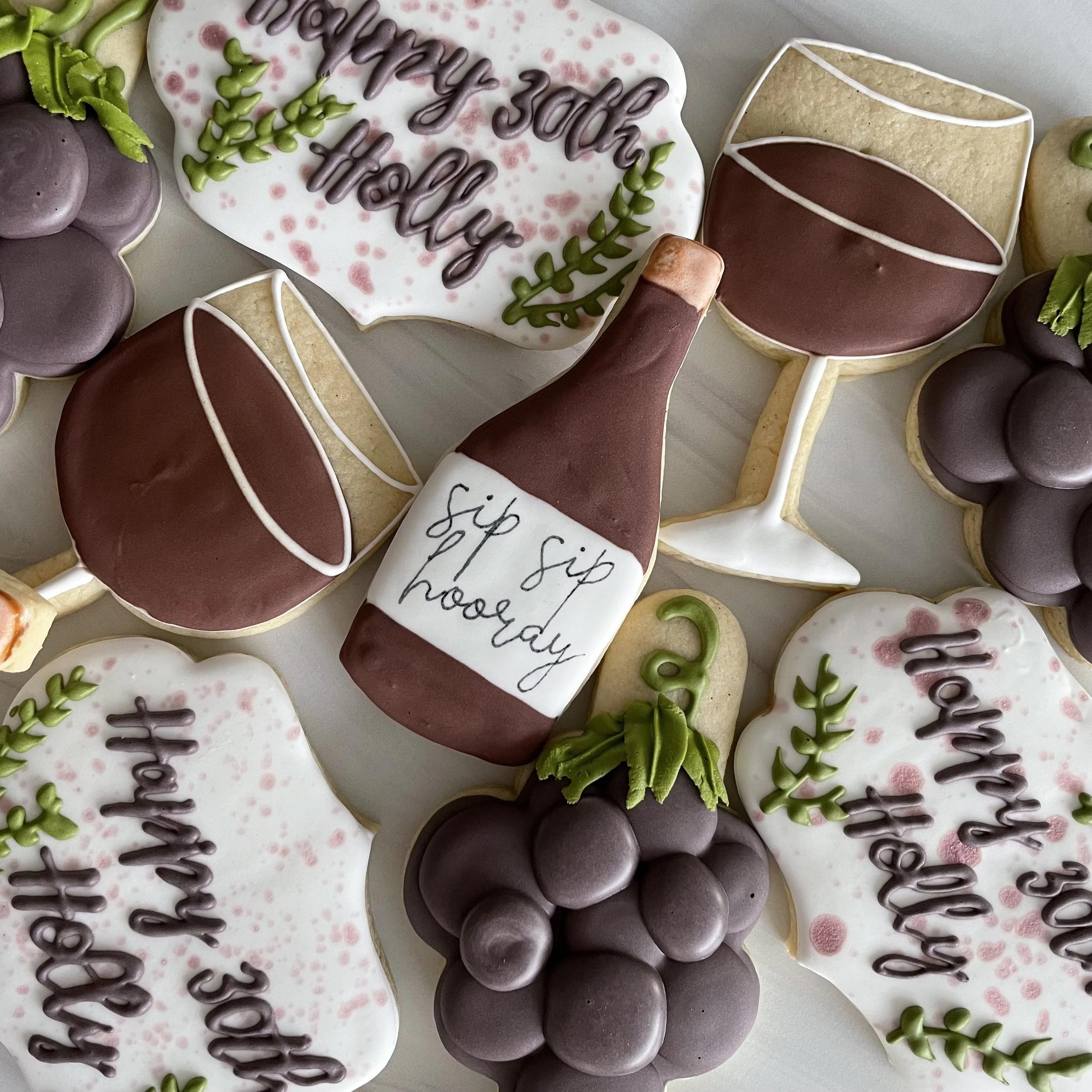 Assorted decorated cookies, some with pink and white icing, green and purple decorative icing, and messages written in icing, with a focus on a white cookie that says "happy 30th birthday."