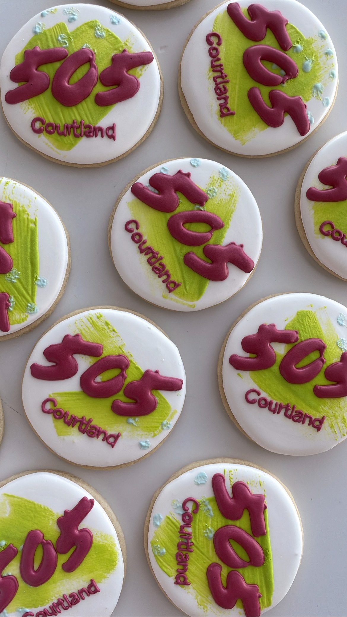 Decorative cookies with white icing, a green painted background, pink icing numbers and words, and small blue sugar dots.