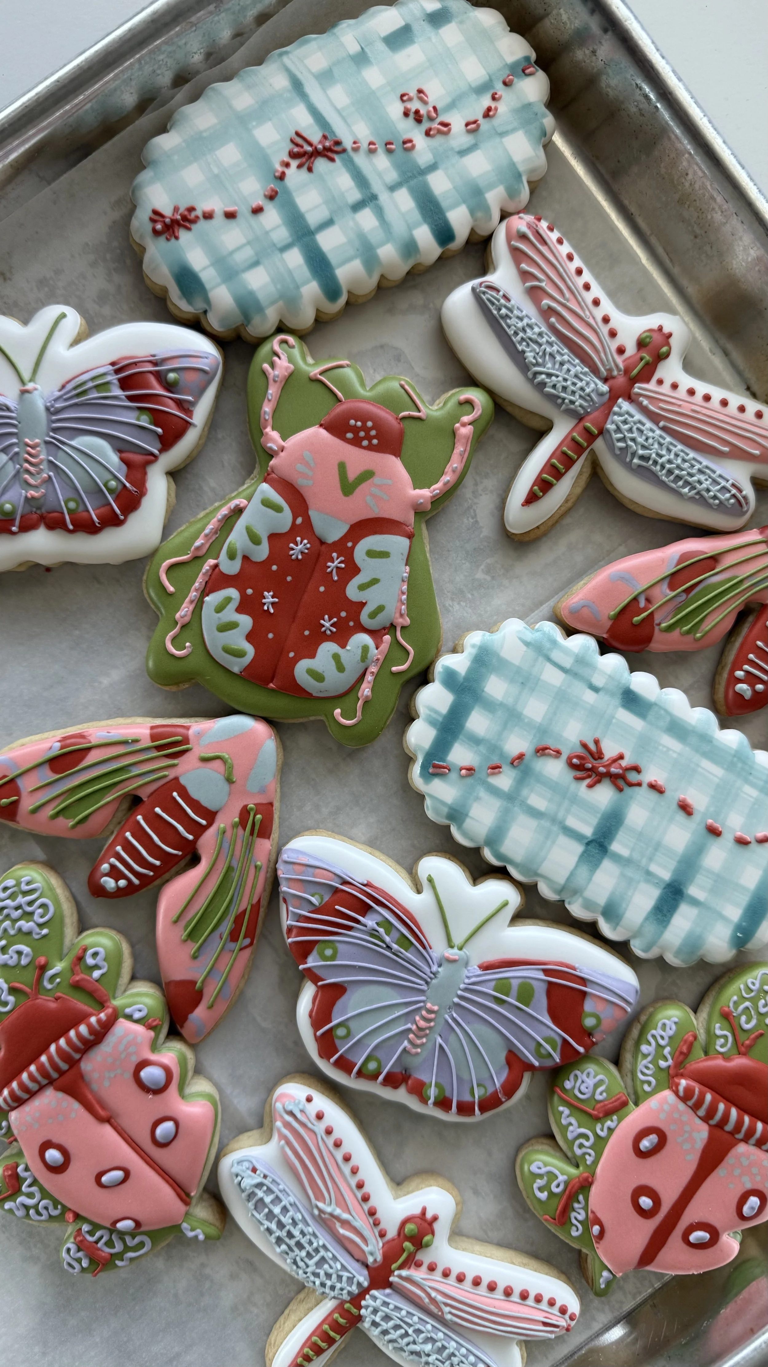 Assorted decorated holiday cookies, including butterflies, ladybugs, and Christmas-themed patterns, on a baking tray.